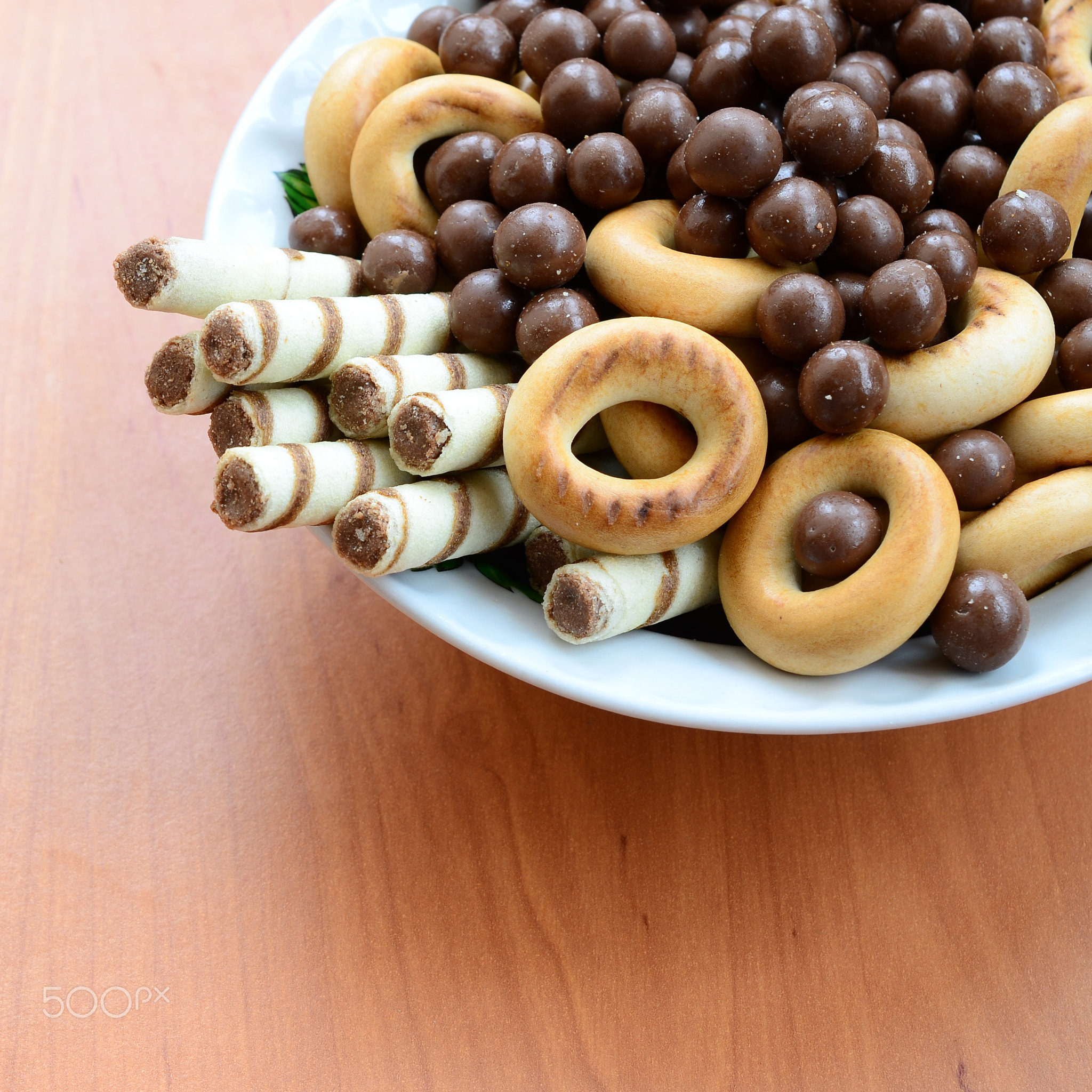 Crispy tubules, chocolate melting balls and bagels lie in a white plate on a wooden table. Mix of