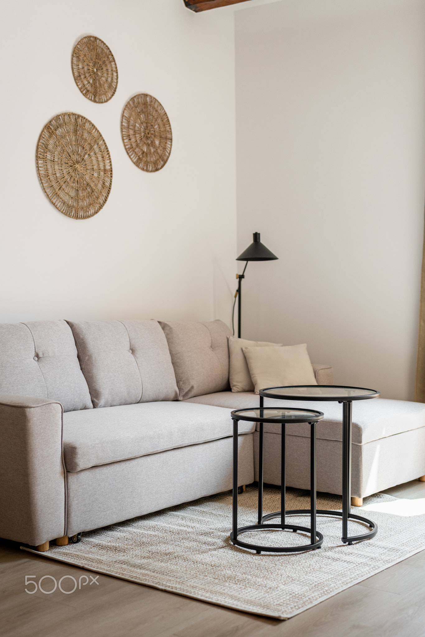 Vertical shot of a beige style corner sofa stands on the floor with a coffee table and circle wall