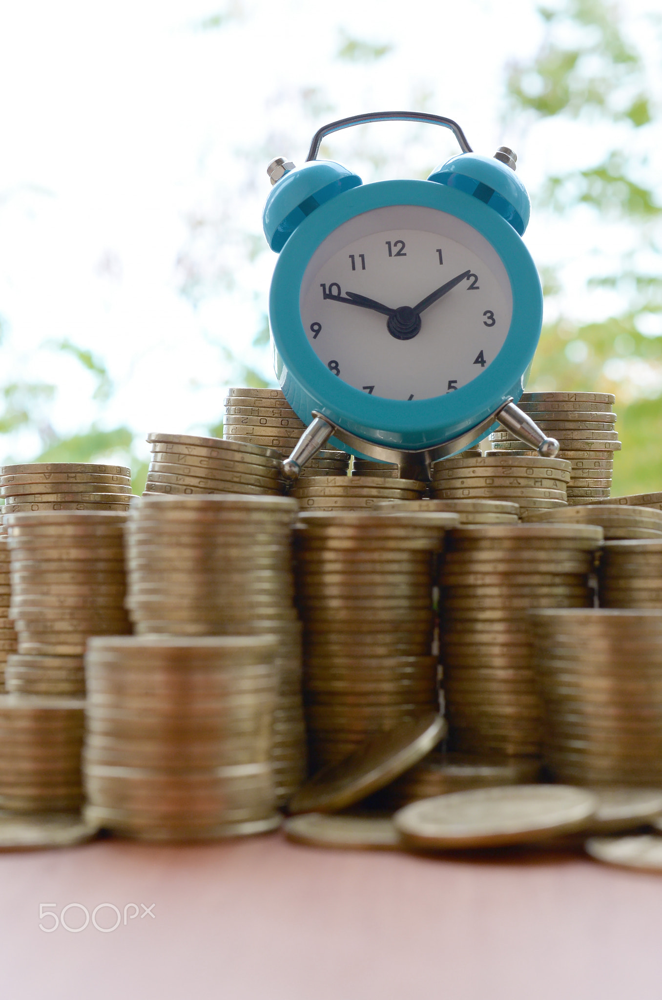 Blue alarm clock on big amount of shiny ukrainian old 1 hryvnia coin stacks close up on blurred