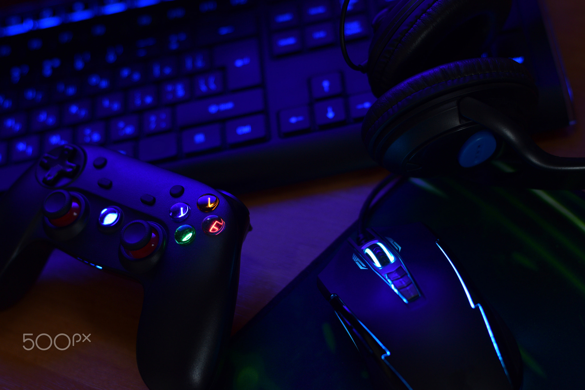 Modern gamepad and gaming mouse lies with keyboard and headphones on table in dark playroom scene