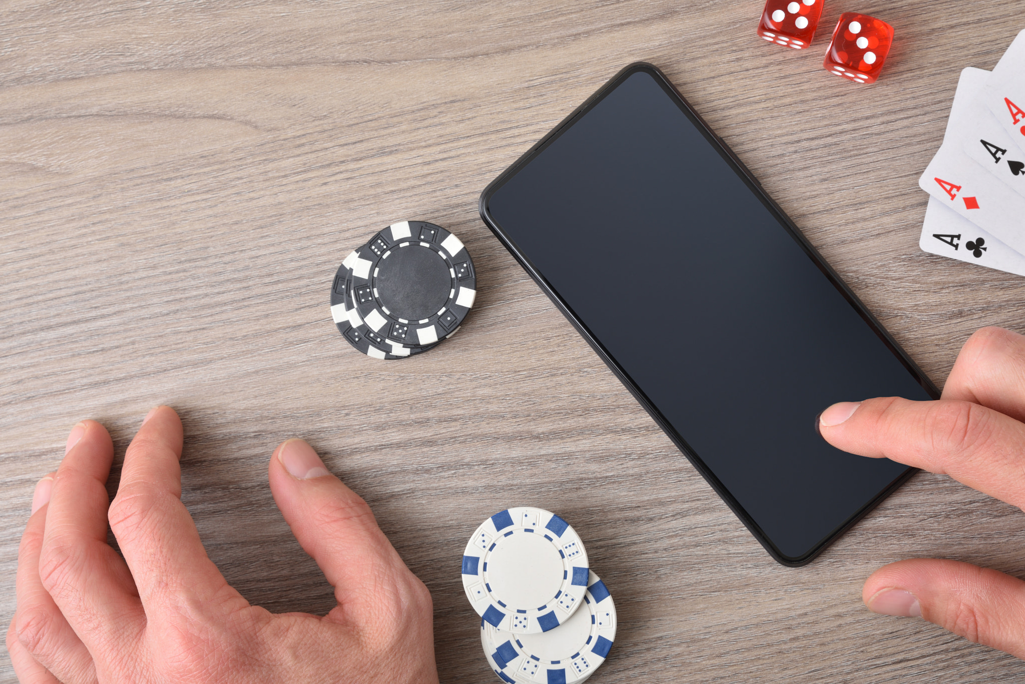 Online gambling concept with hand using smartphone and game pieces