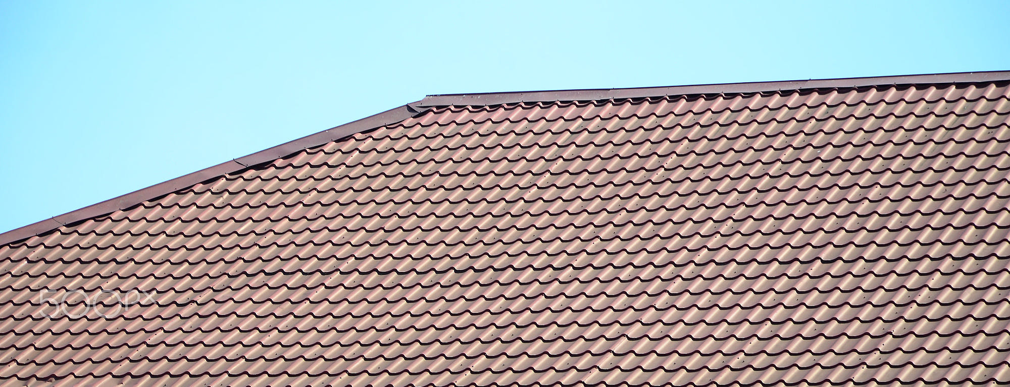 A fragment of a roof from a metal tile of dark red color. Quality Roofing: A fragment of a roof from a metal tile of dark red color. Quality Roofing