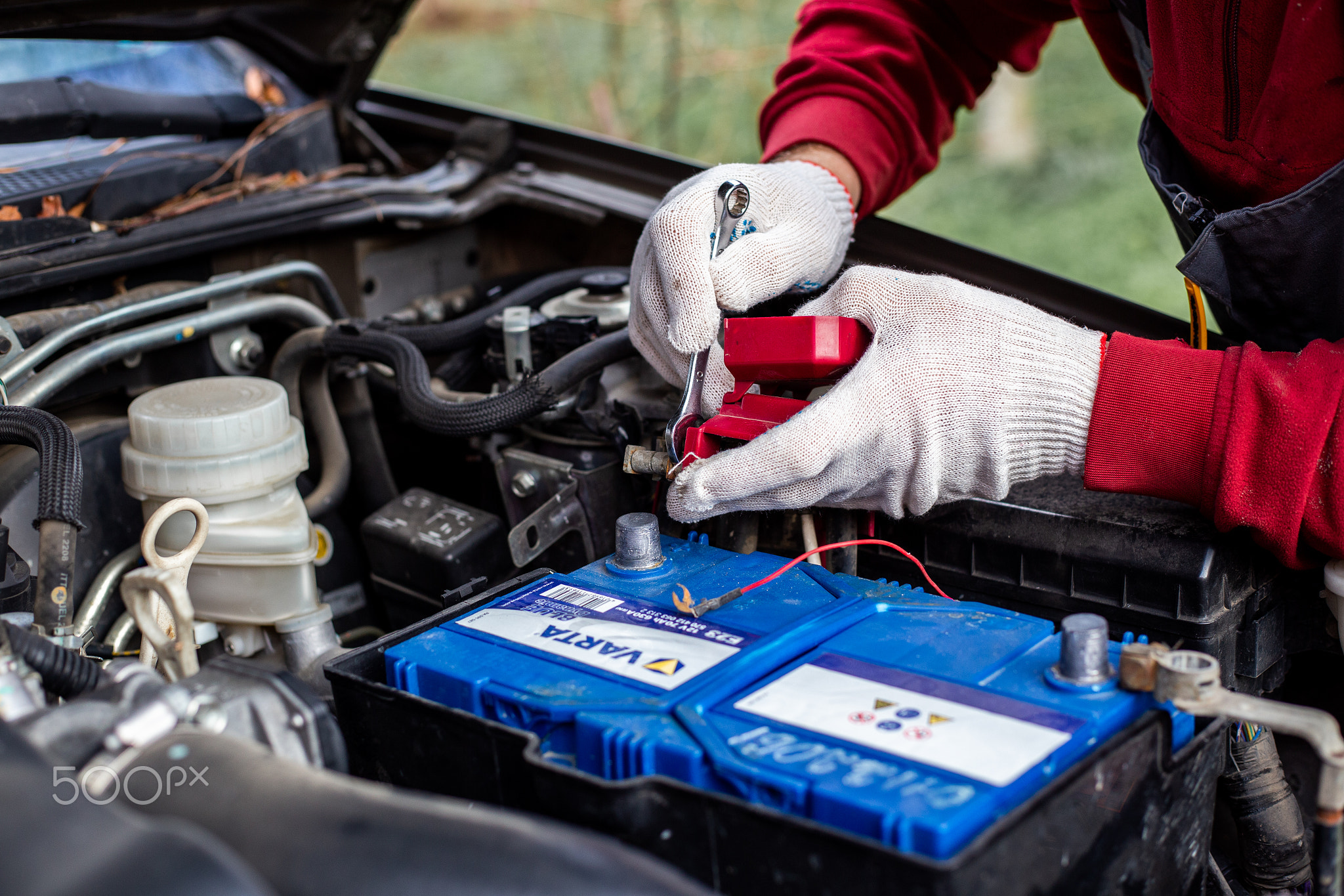 A man screws the terminals of Varta car battery under the hood of the