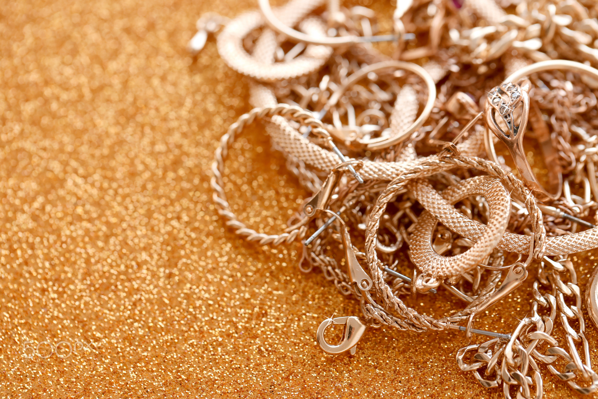 Many expensive golden jewerly rings, earrings and necklaces on golden glitter background with shiny