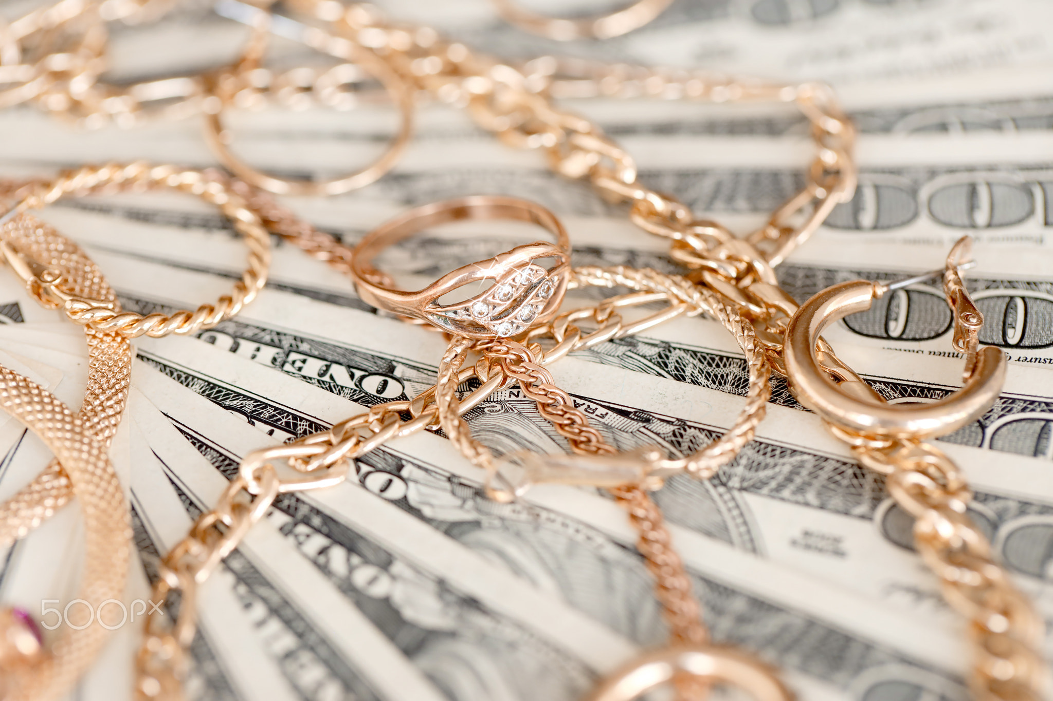 Many expensive golden jewerly rings, earrings and necklaces on big amount of US dollar bills close