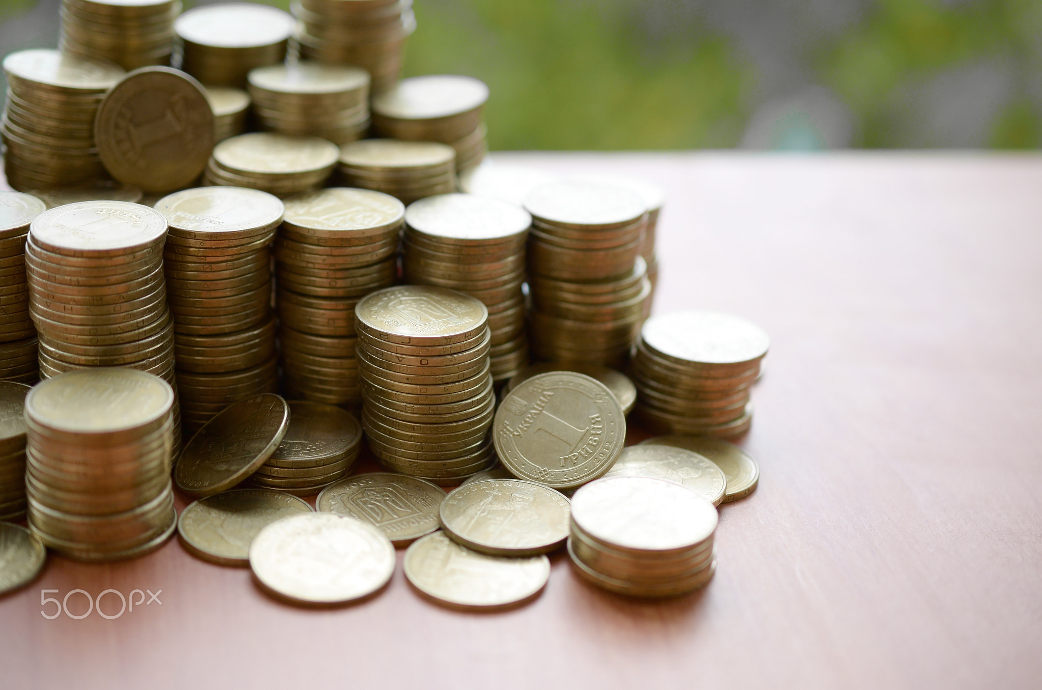 Big amount of shiny ukrainian old 1 hryvnia coin stacks close up on wooden table on green trees