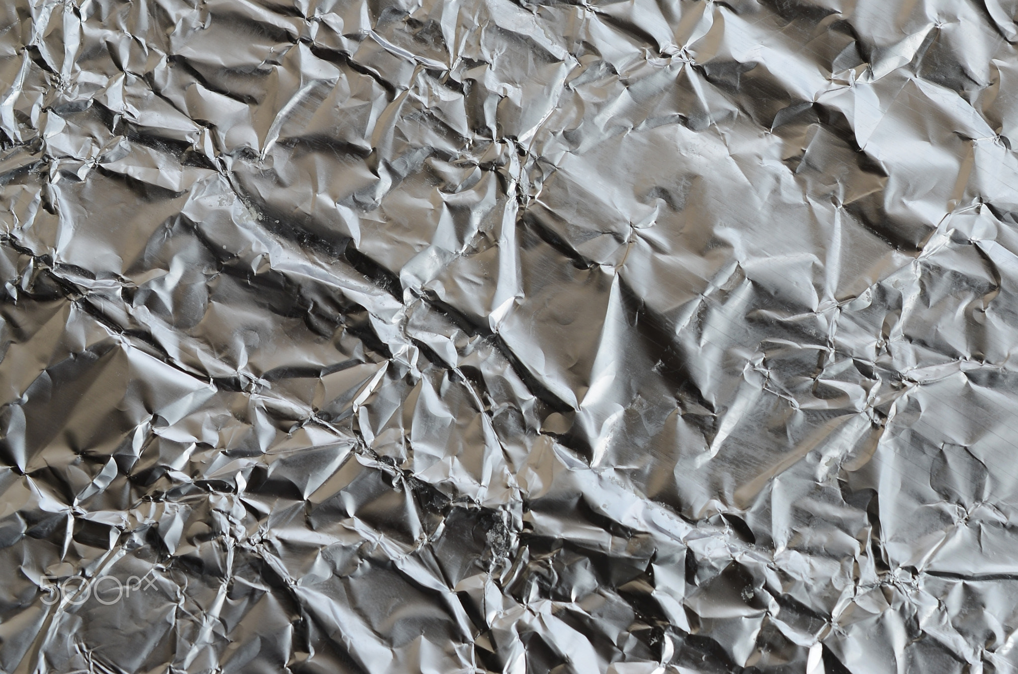 Thin wrinkled sheet of crushed tin aluminum silver foil background with shiny crumpled surface for