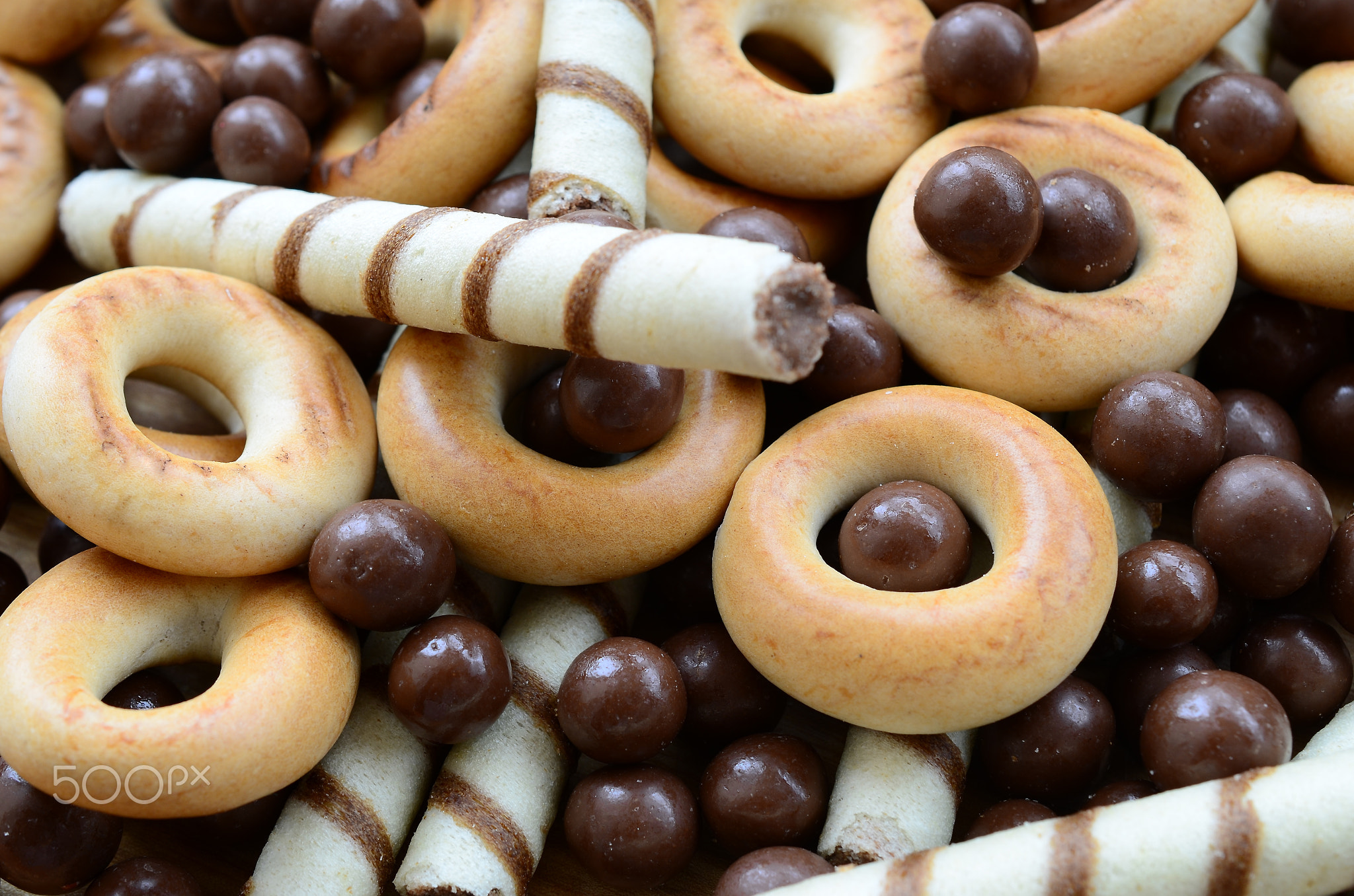 A lot of crispy sweet tubules, chocolate melting balls and yellow bagels lie on a wooden surface