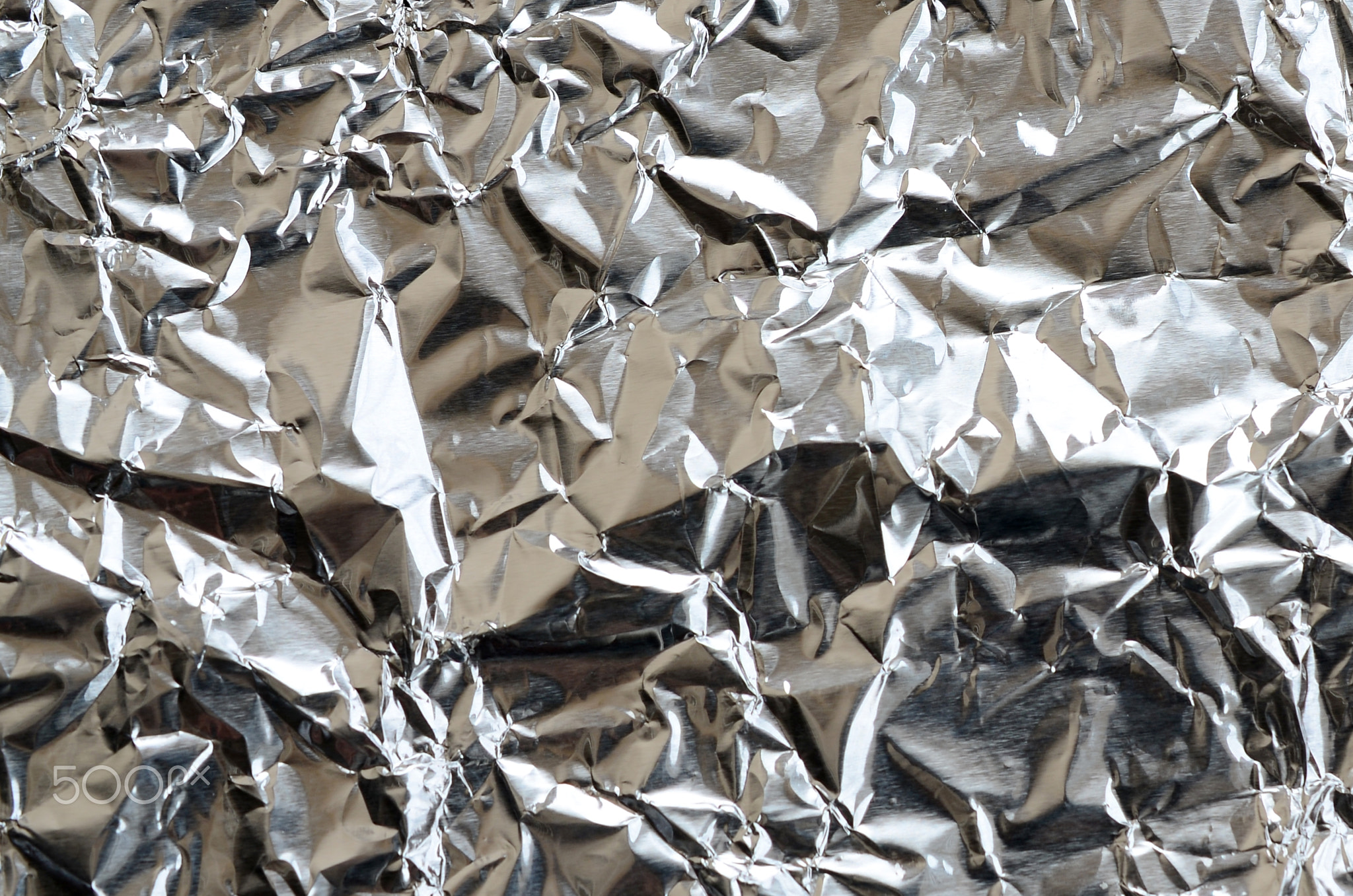 Thin wrinkled sheet of crushed tin aluminum silver foil background with shiny crumpled surface for