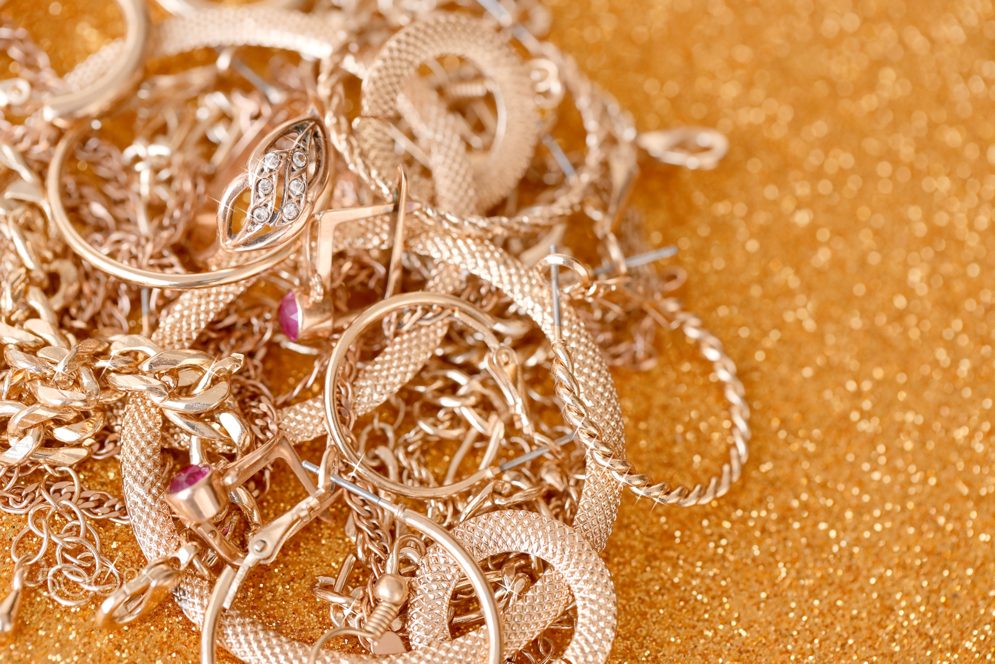 Many expensive golden jewerly rings, earrings and necklaces on golden glitter background with shiny