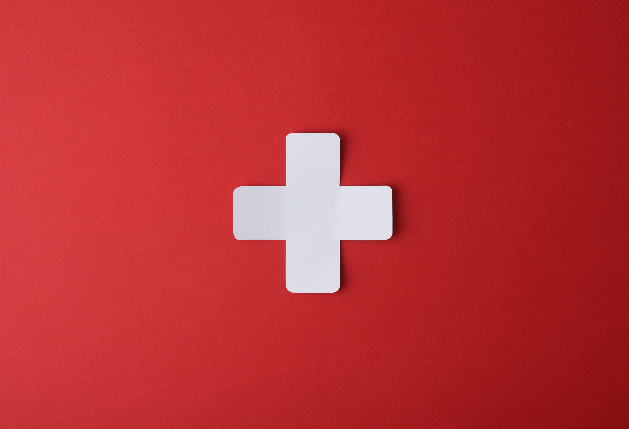 Conceptual medicine symbol with cross cutout on red background: Conceptual medicine symbol with cross shaped paper cutout isolated in the center on red background.