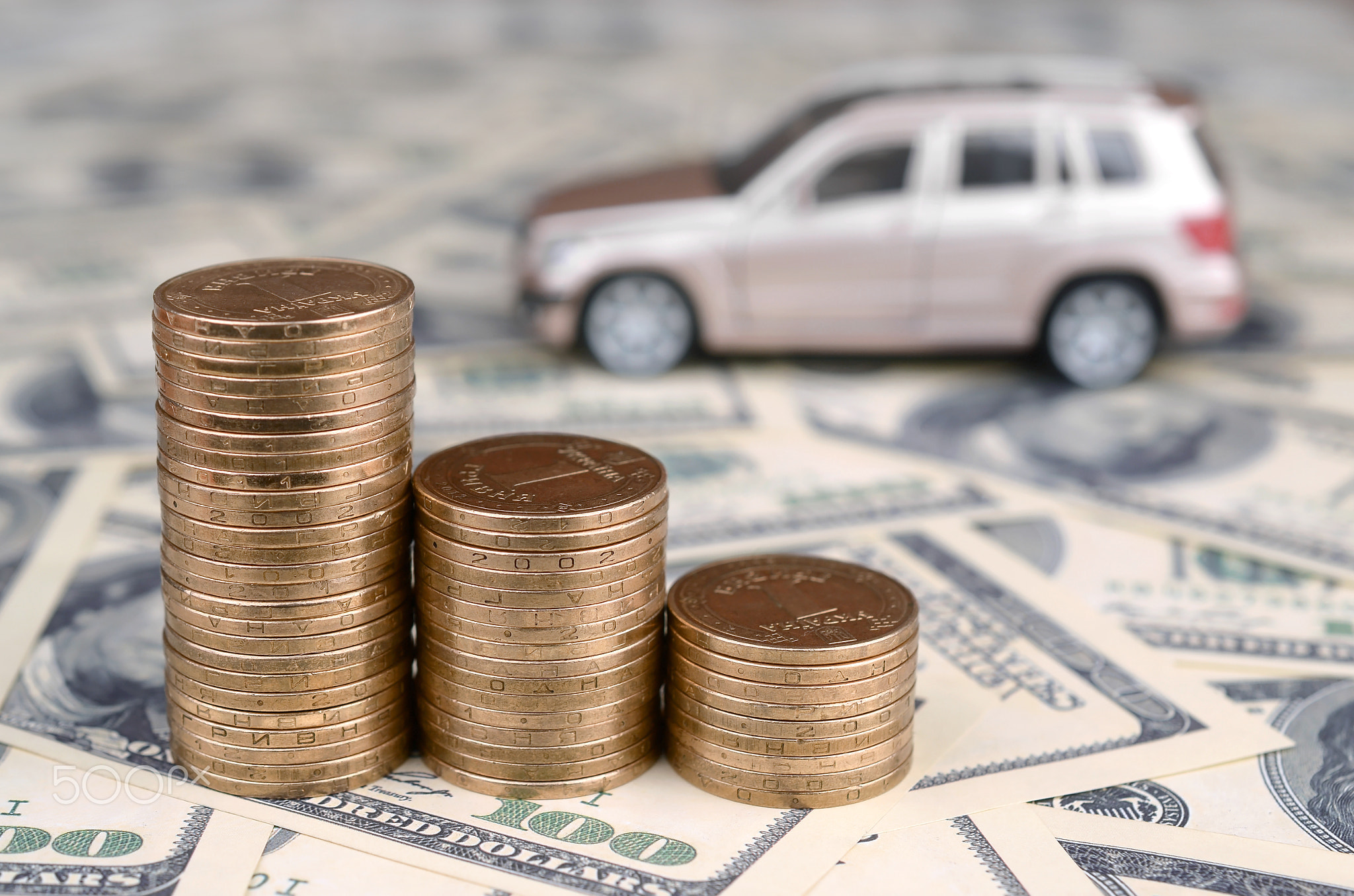 Toy car model at the stacks of golden coins lies on many dollar bills