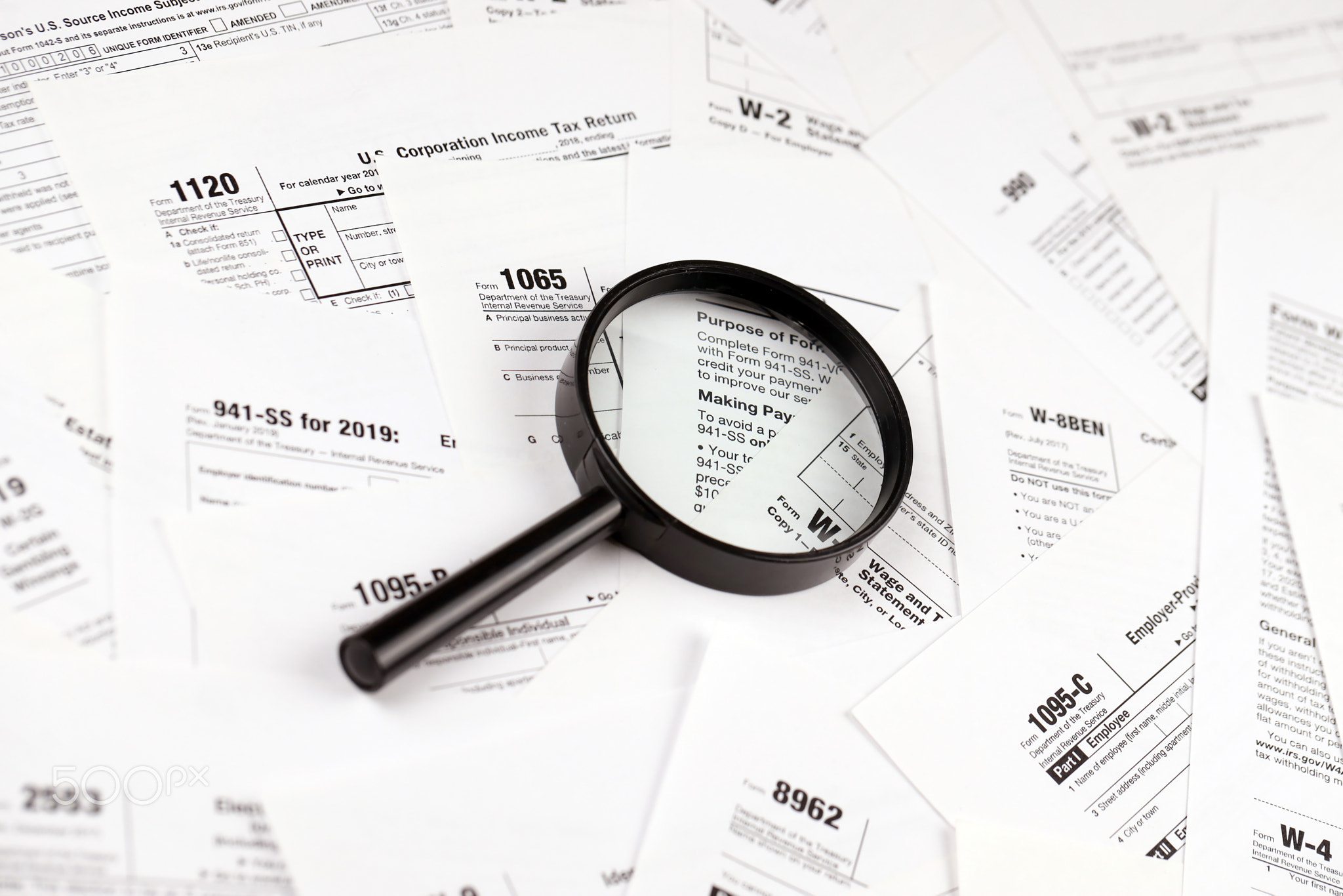 Magnifying glass lying over heap of paper documents. Investigation and financial audit