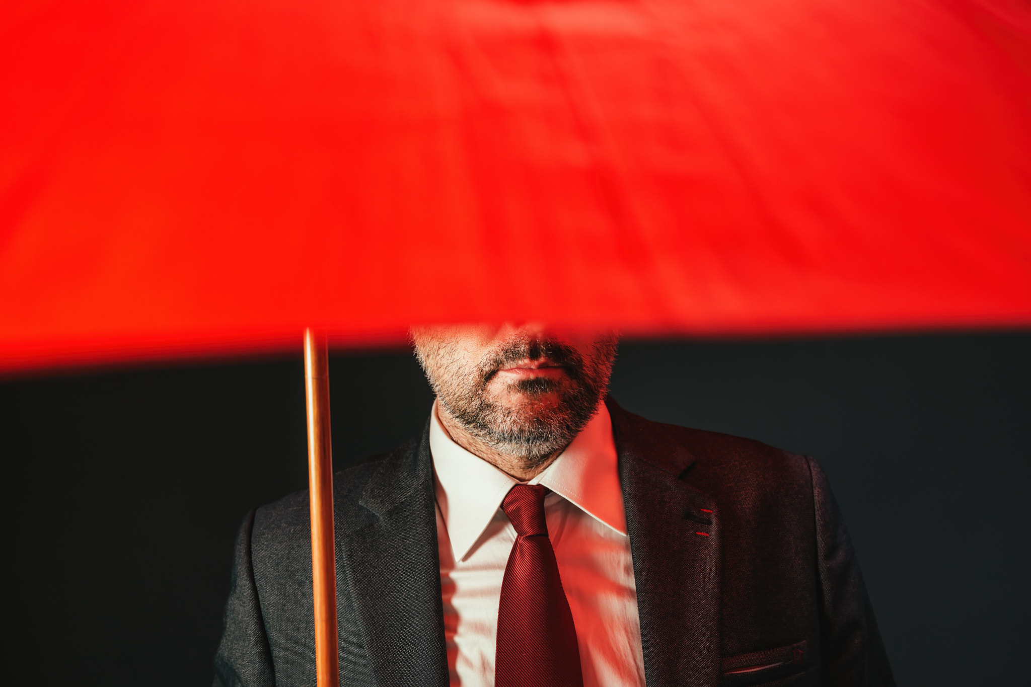 Businessman under red umbrella, low key