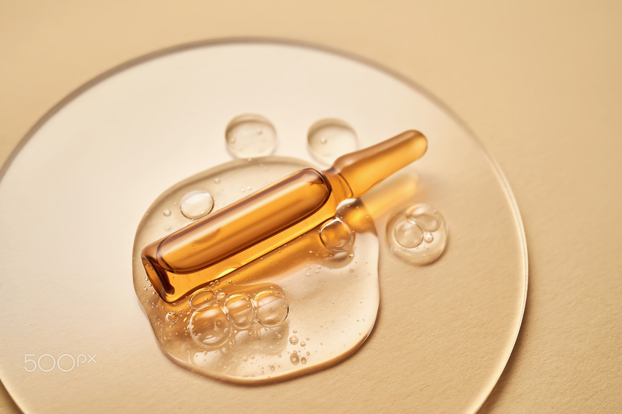 Ampoule in a drop of cosmetic gel on a beige background.