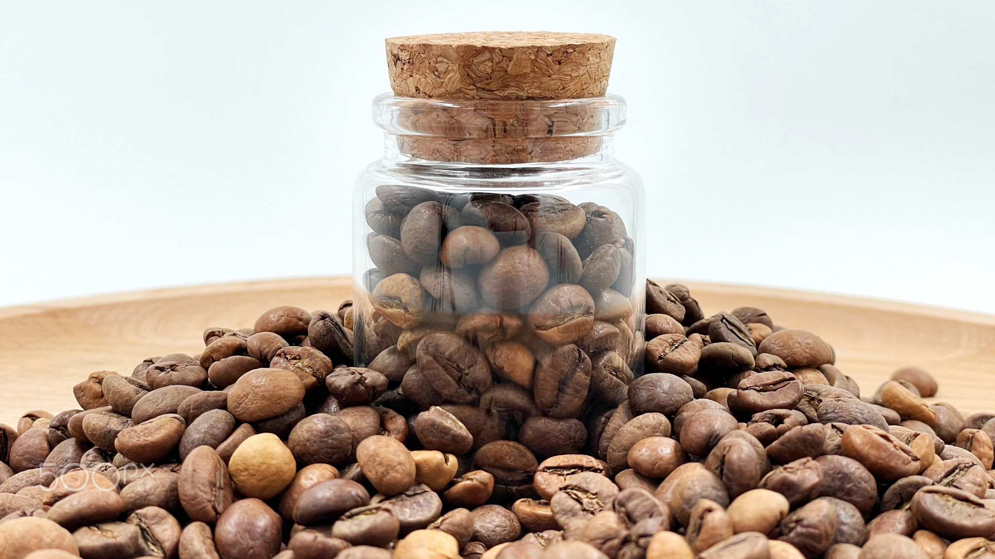 Coffee beans in a small glass jar with a cork lid on the table. Coffee