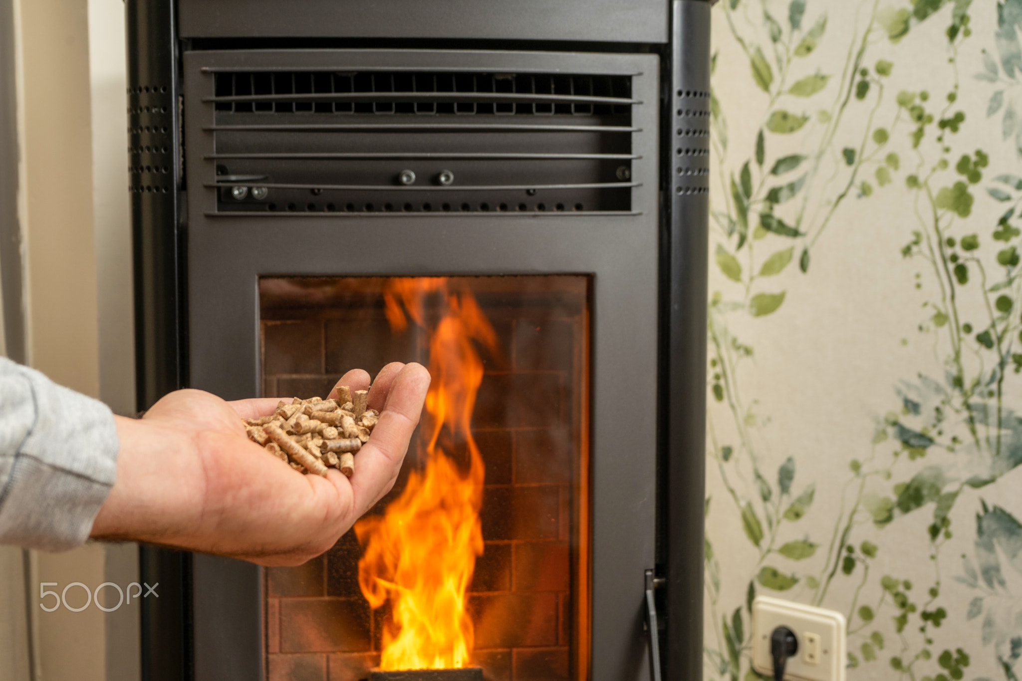 Man's hand holding pellets in front of the glass of a stove with a