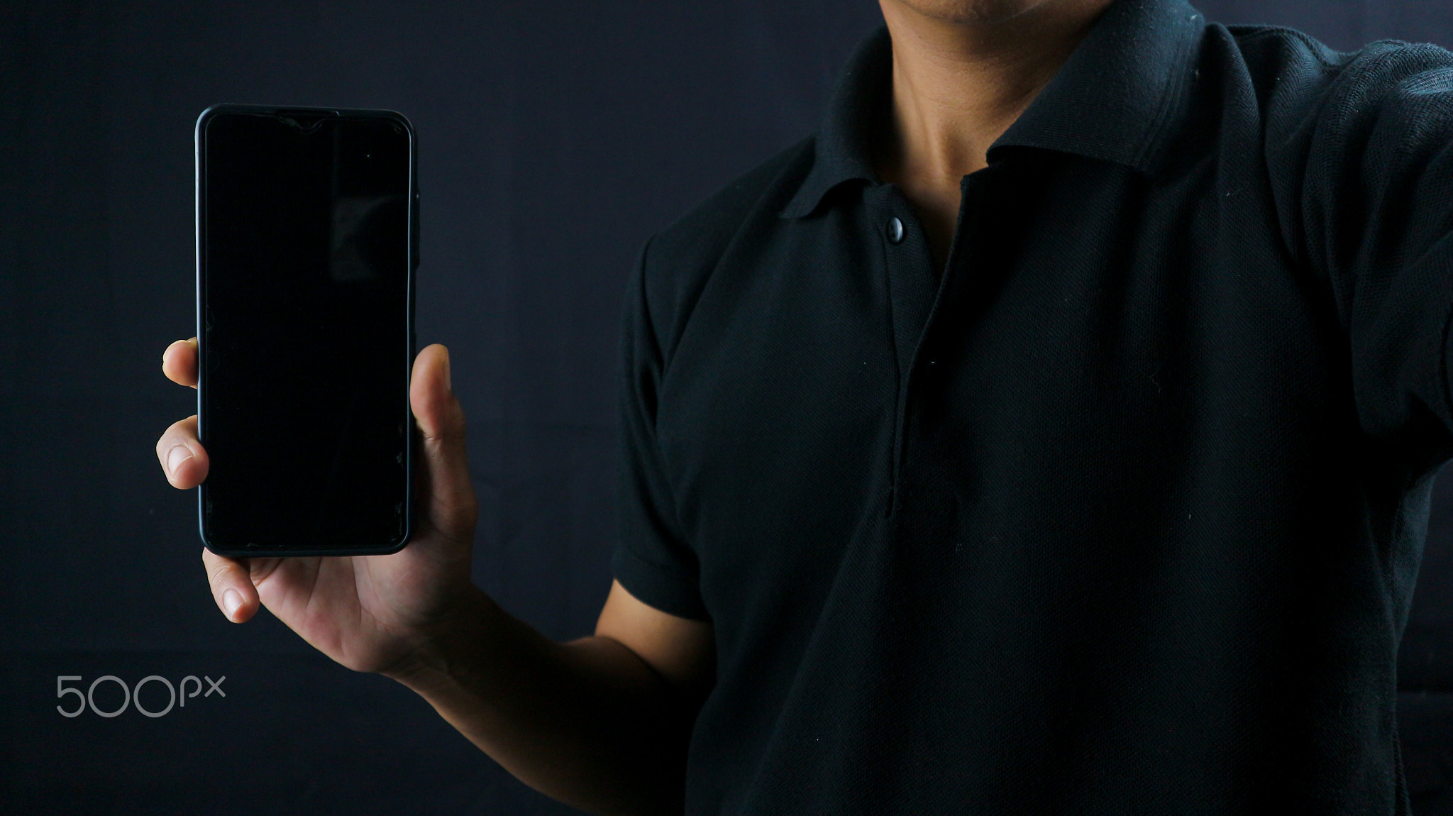 Asian man holding big smartphone with blank screen in hand, showing close to camera and pointing at