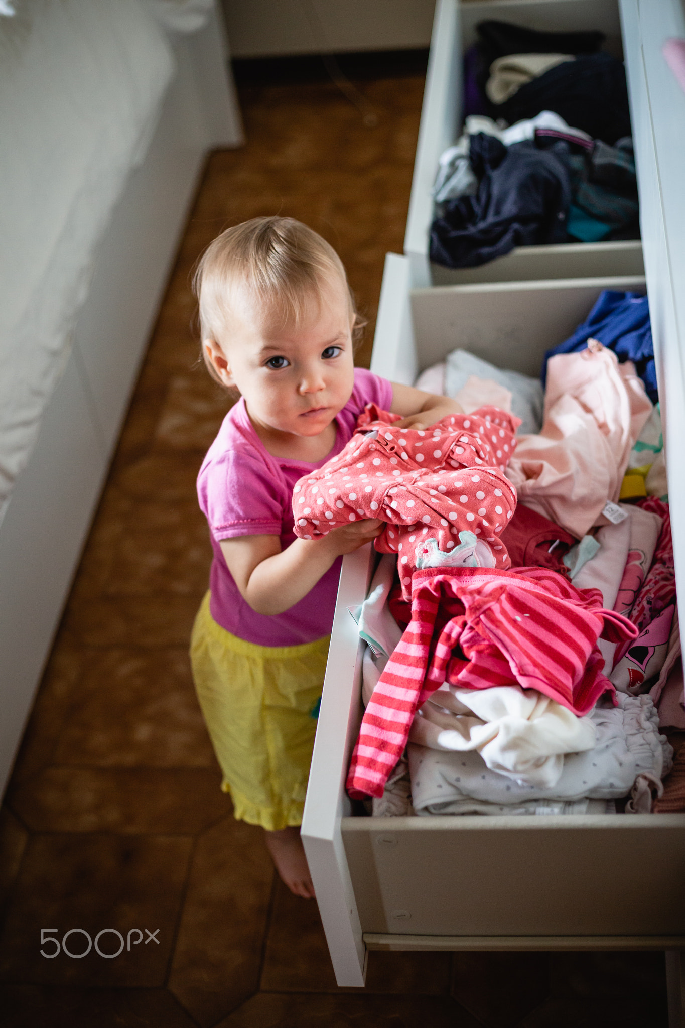 upper view of little baby playing with clothes in the drawers, making order