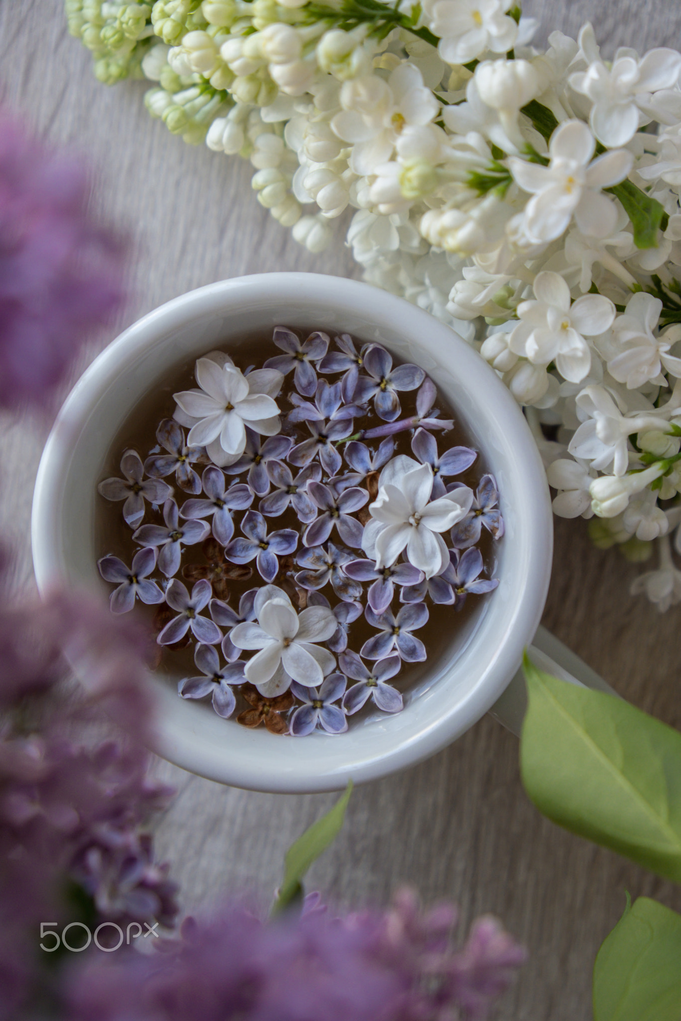 Tasty black tea in white cup on windowsill with aromatic lilac flowers