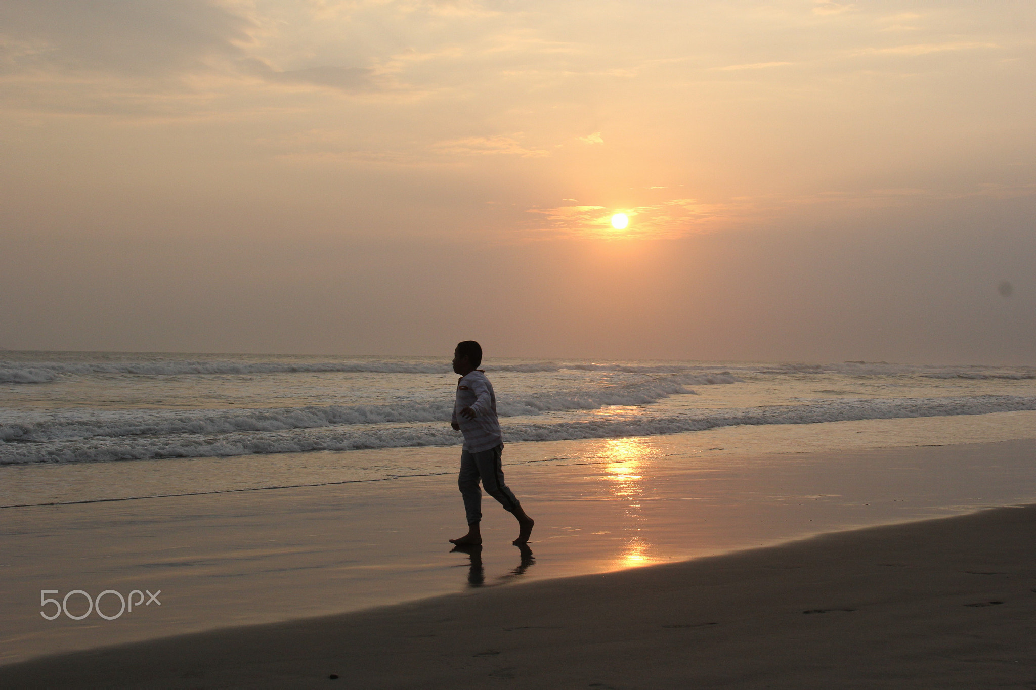 Full length of boy running on shore at beach against sky during sunset