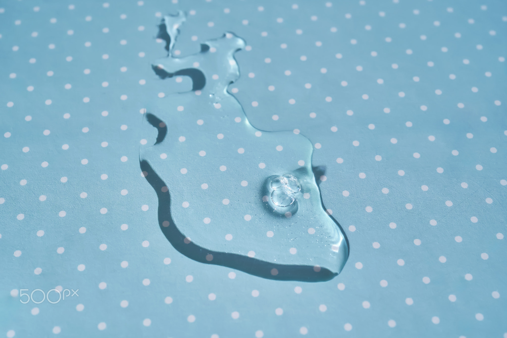 A drop of water or cosmetic serum on a blue polka dot background.