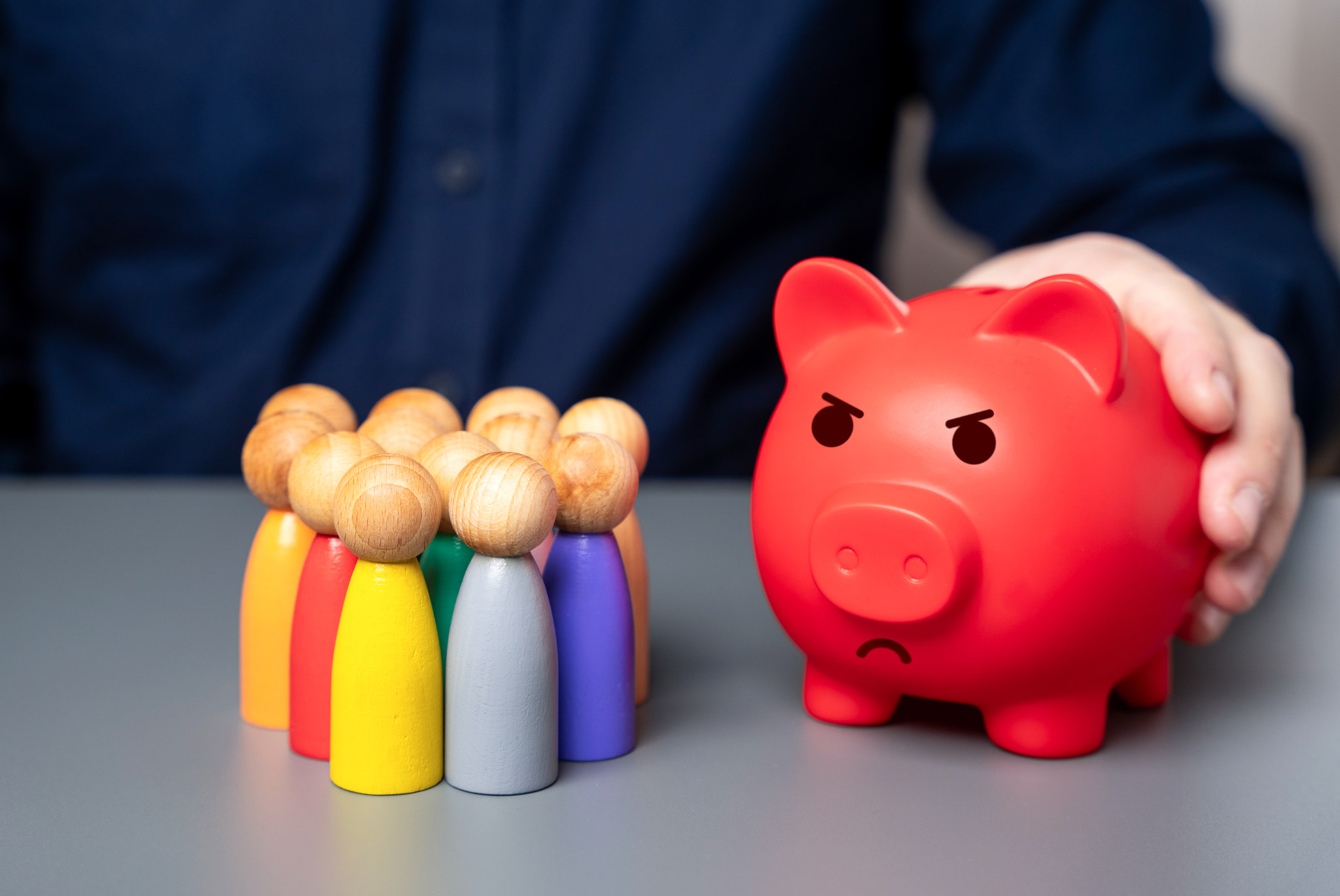 A businessman holds a red piggy bank next to a group of people figures. Lack of budget funds. Poor d