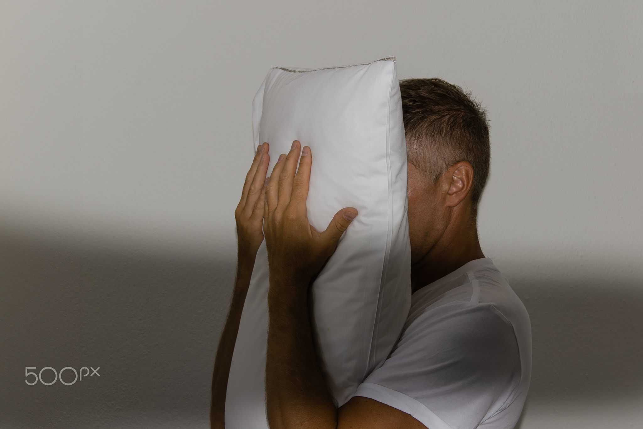 Insomnia and man covers his face with pillow.