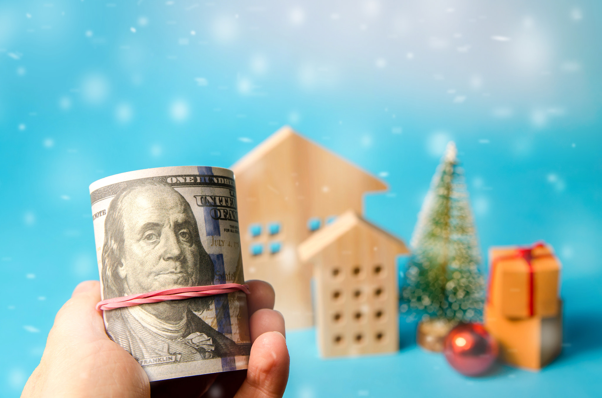 Dollars in hand on background wooden houses, christmas tree and gifts. Christmas and new year prepar