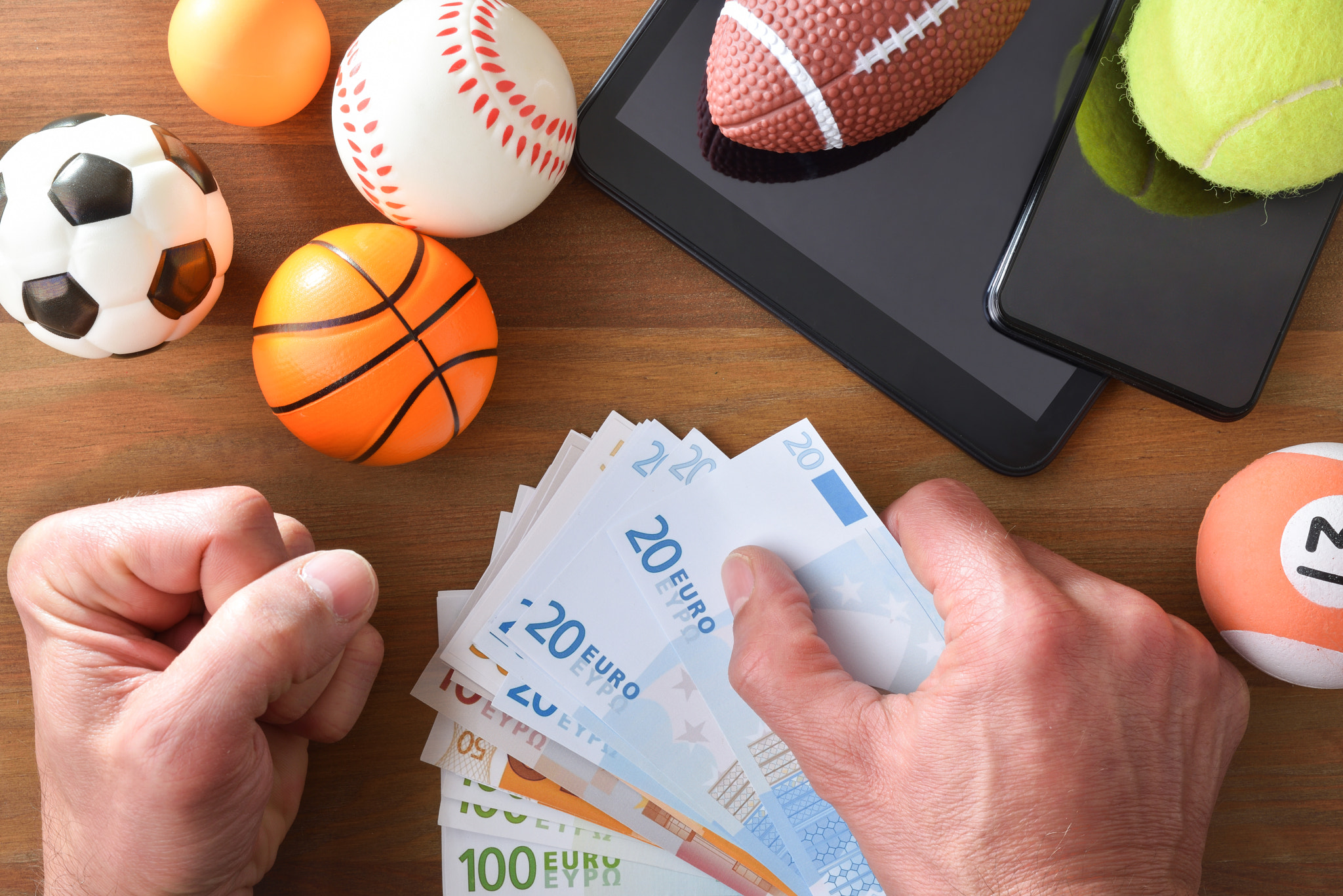 Man betting online with devices on wooden table and objects