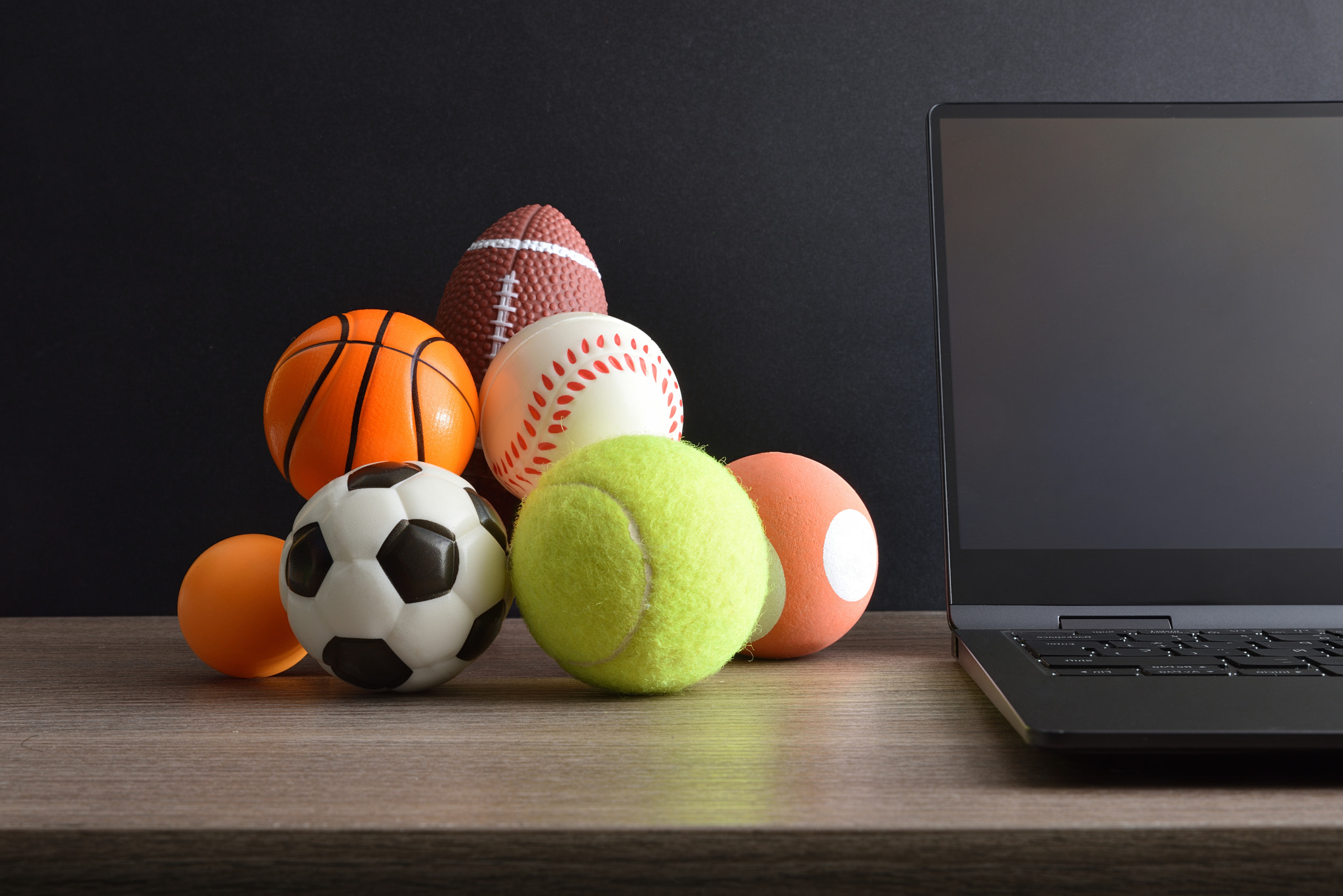 Concept of sports entertainment on internet with laptop and balls: Concept of sports entertainment on the internet with a laptop and balls of various sports on an office table. Front view.