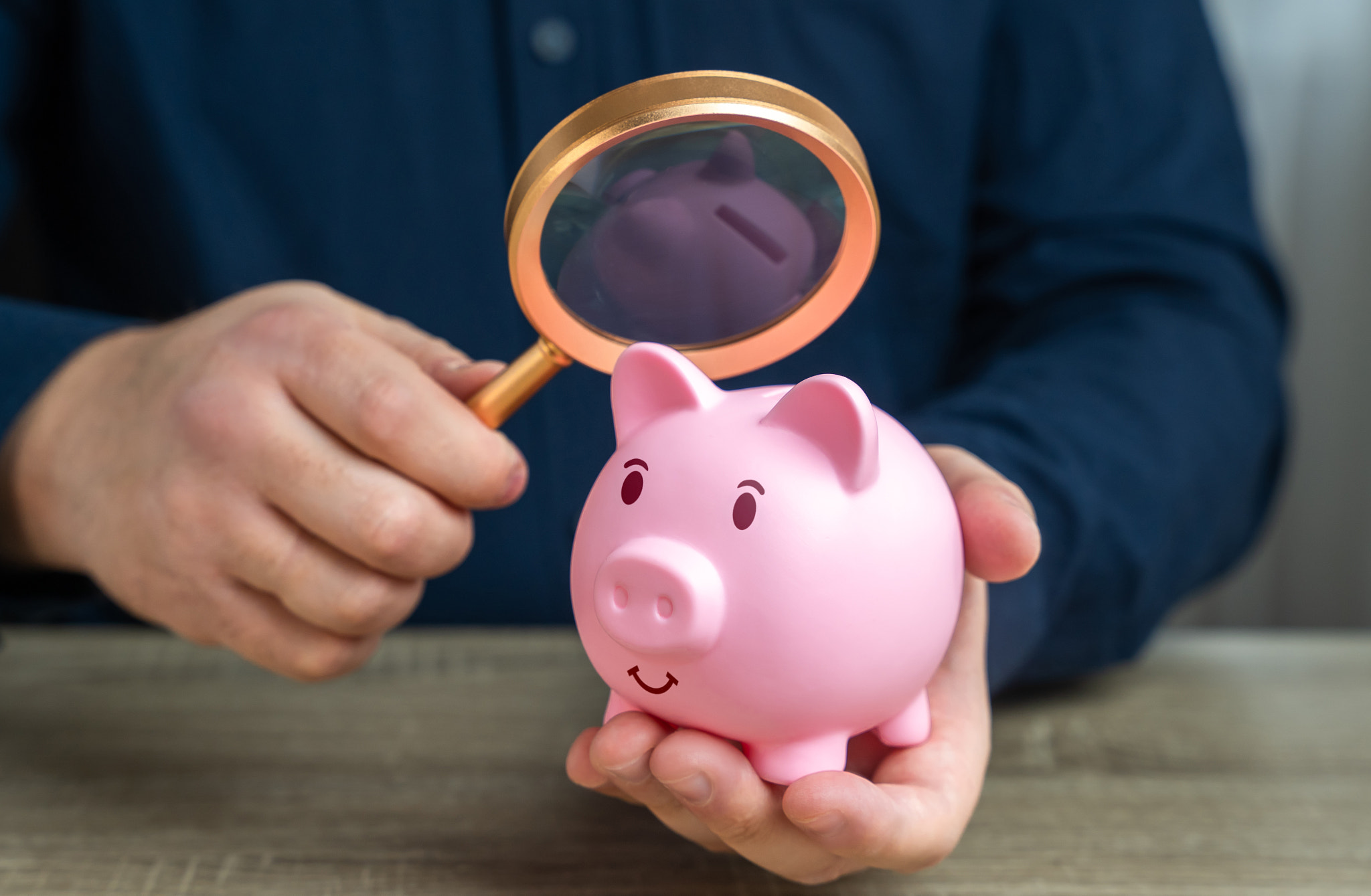 A man looks at a piggy bank with a magnifying glass. Investigating capital origins. Anti money laund