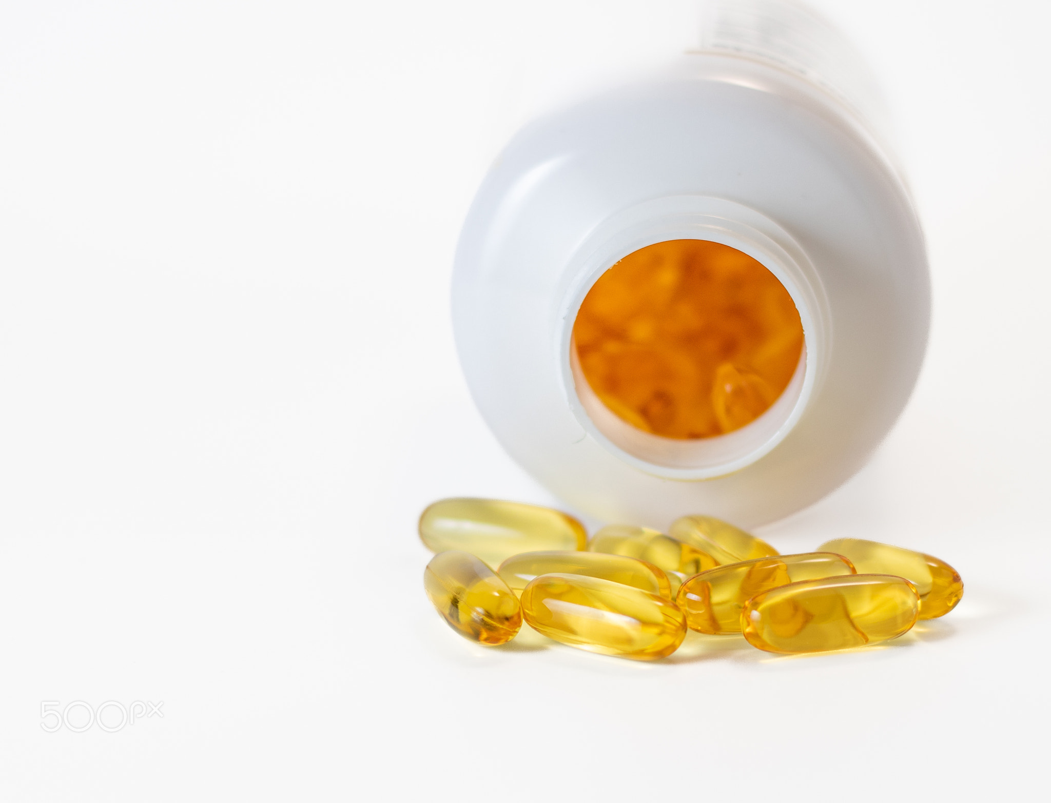 Yellow fish oil capsules in a jelly shell near the white jar