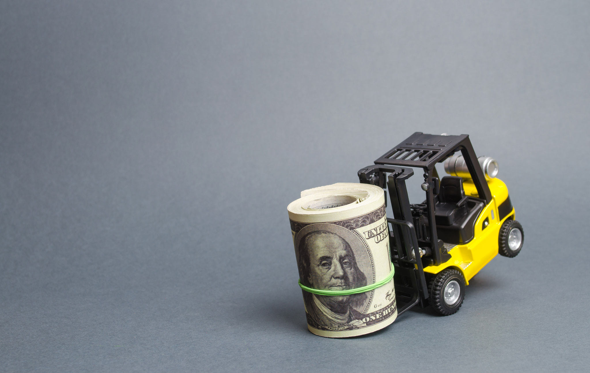 Yellow forklift truck can't lift a huge bundle of dollars. Expensive loans, high tax burden. attract