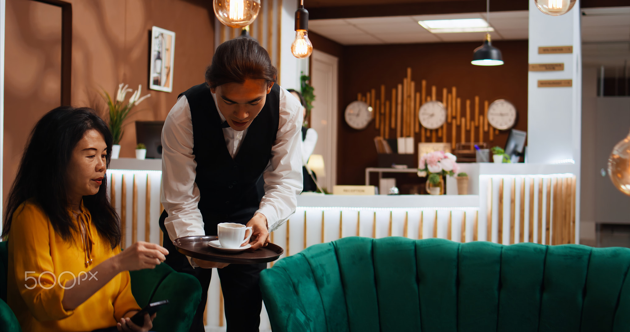 Asian waiter bringing coffee to guest in lounge area