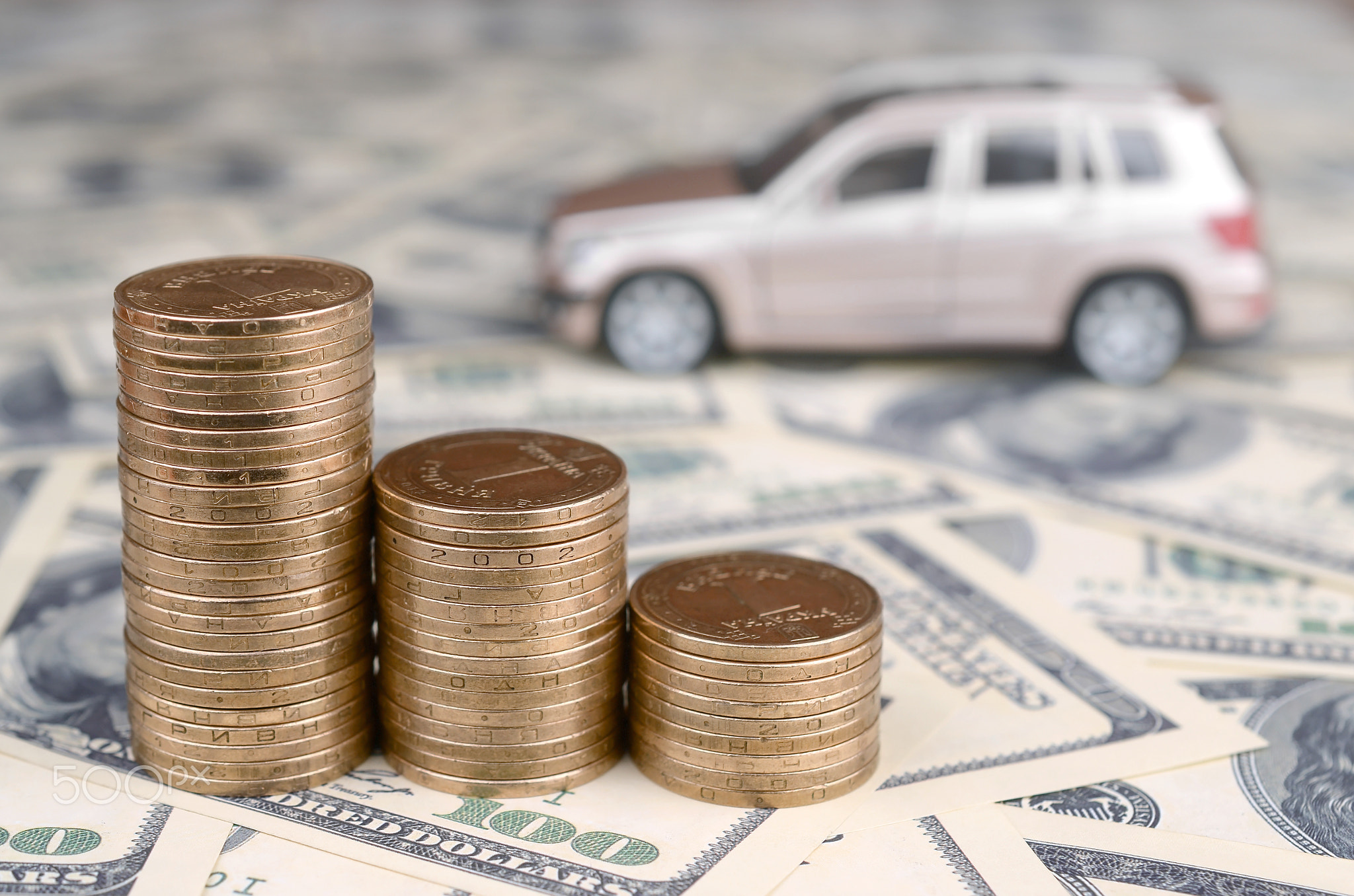 Toy car model at the stacks of golden coins lies on many dollar bills