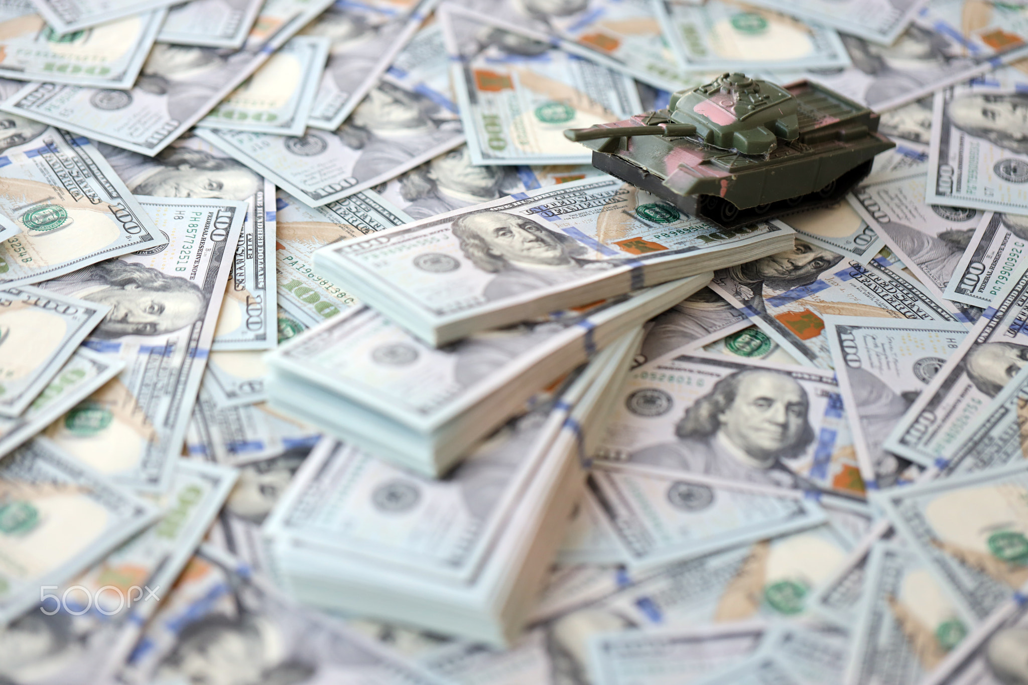 Toy tank on US hundred dollar bills banknotes. The concept of war costs, military spending and