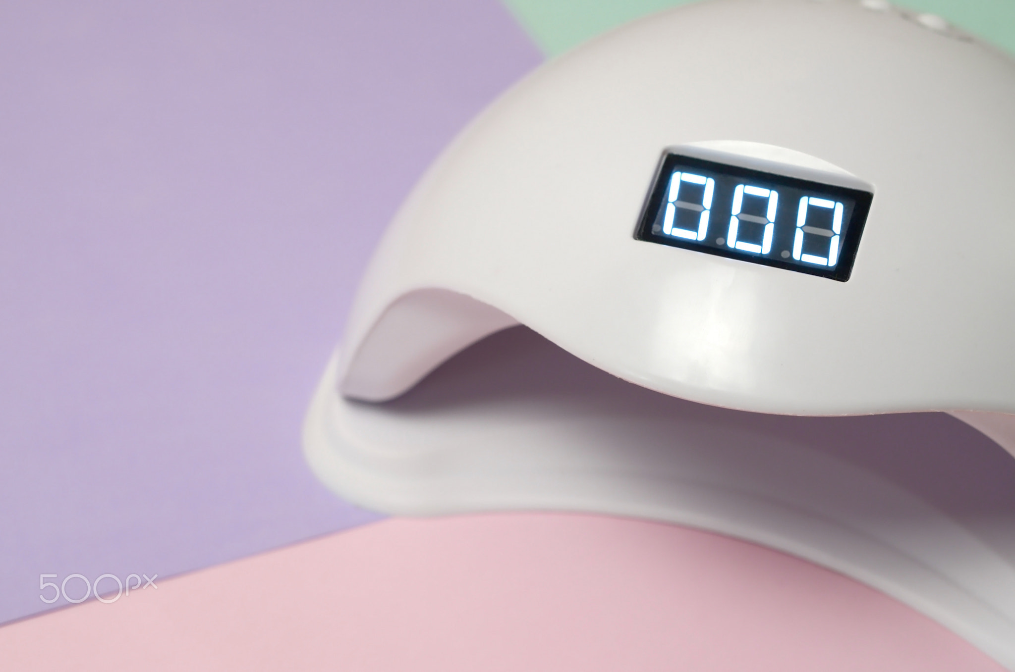 UV LED nail lamp for curing process by gel method lies on pastel multi colored table