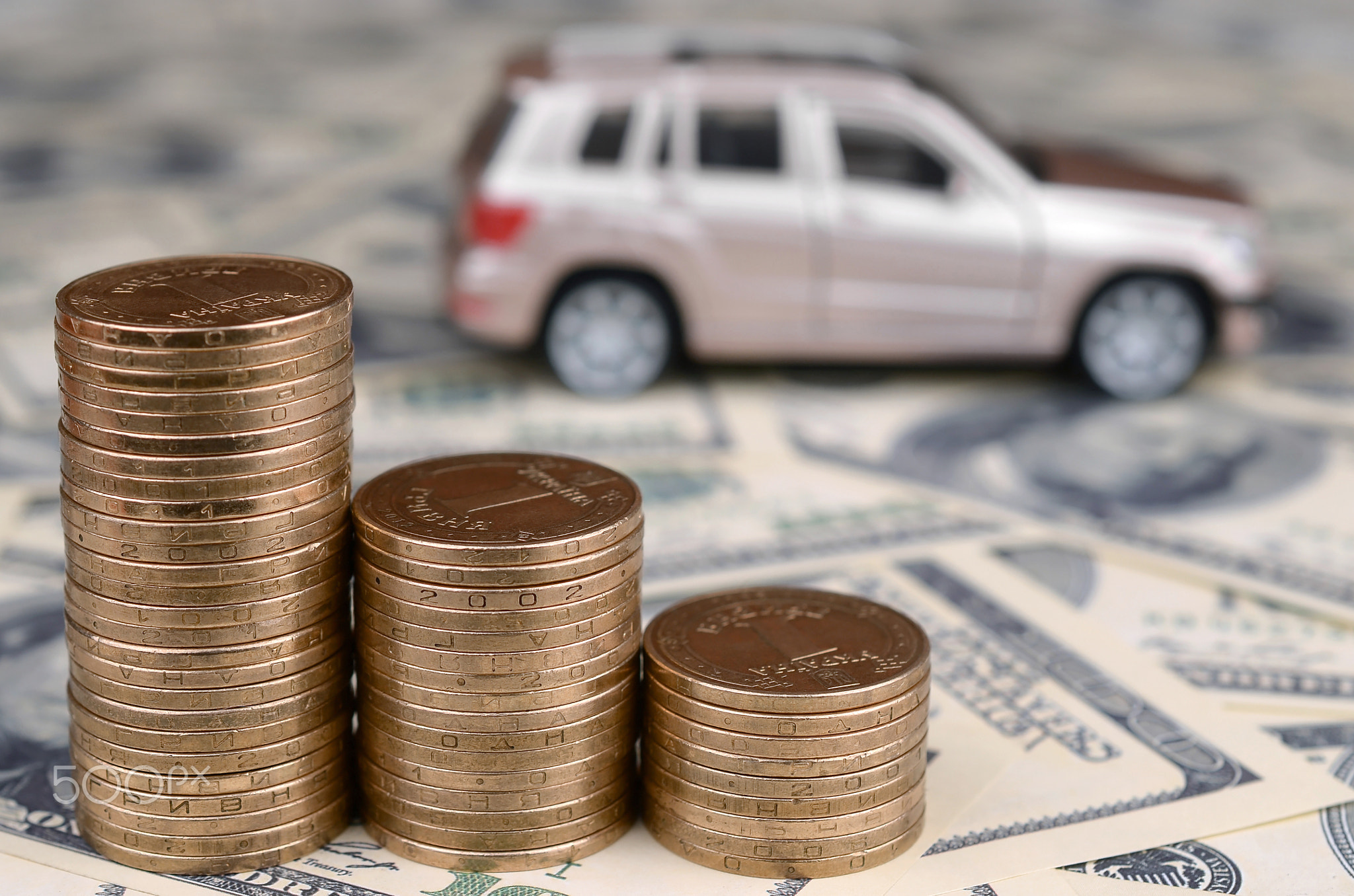 Toy car model at the stacks of golden coins lies on many dollar bills