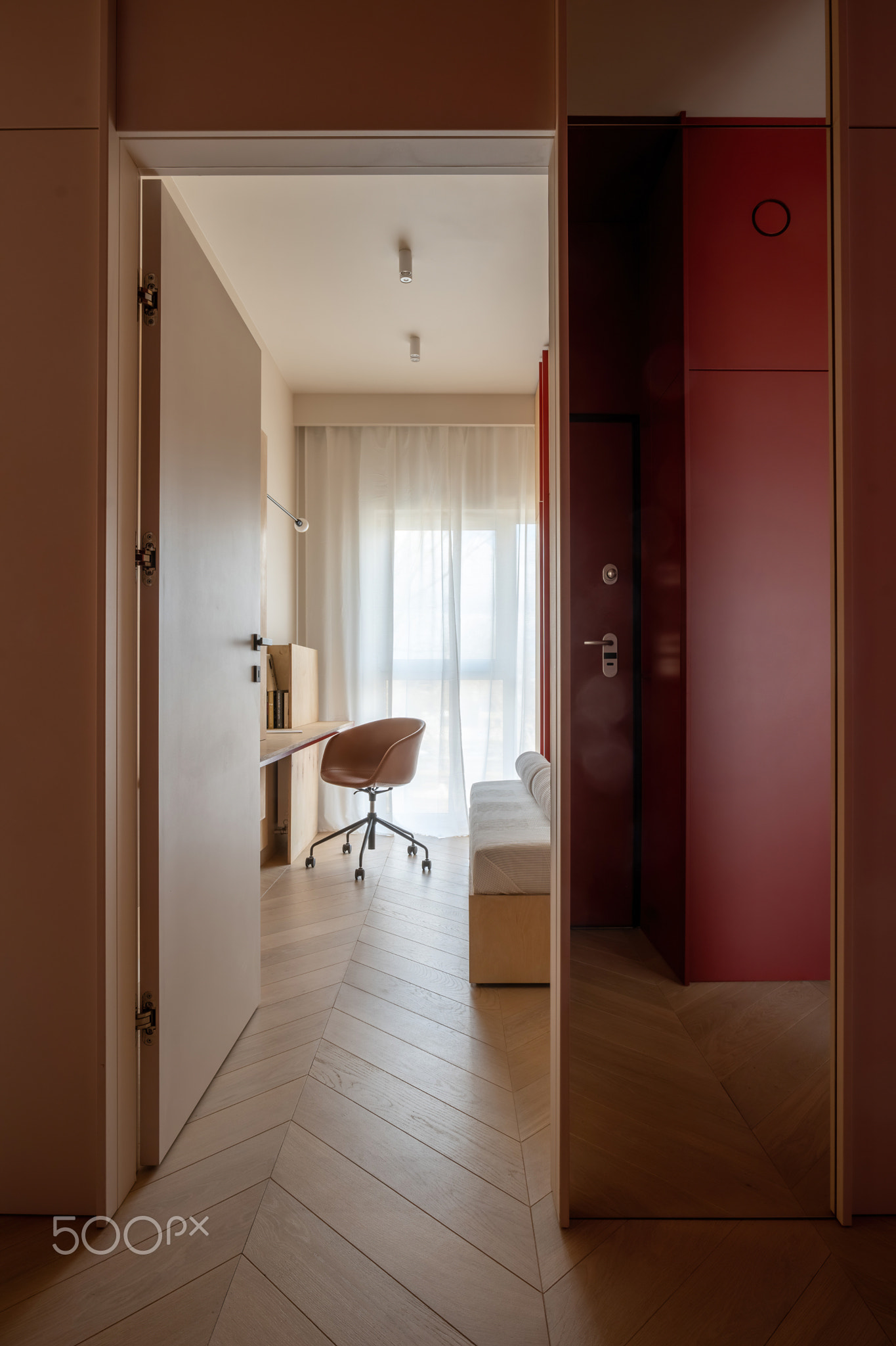 Hallway with hardwood flooring leads to bedroom with desk and chair