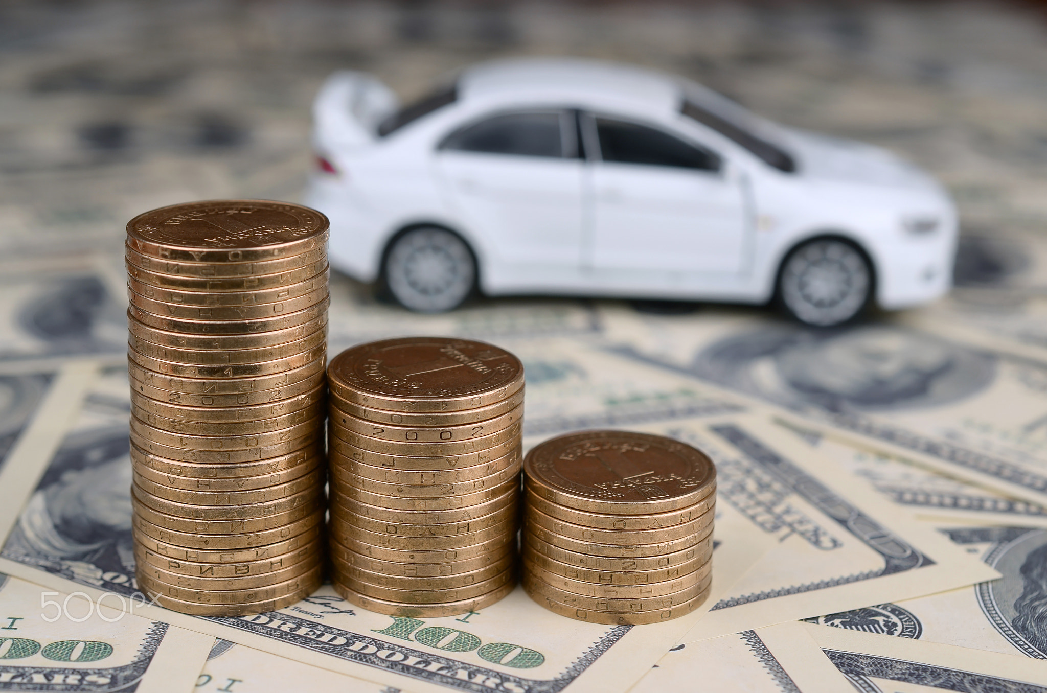 Toy car model at the stacks of golden coins lies on many dollar bills