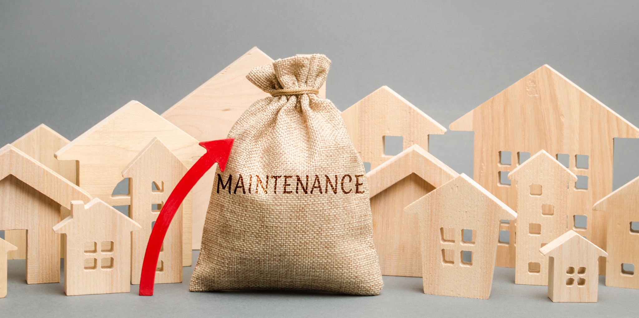 A bag with the word Maintenance, wooden houses and up arrow. Rising costs for the maintenance of hou
