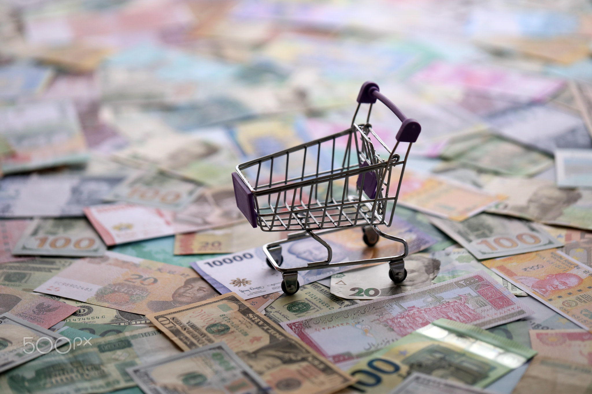 Supermarket trolley on many banknotes of different currency. Background of shopping worldwide