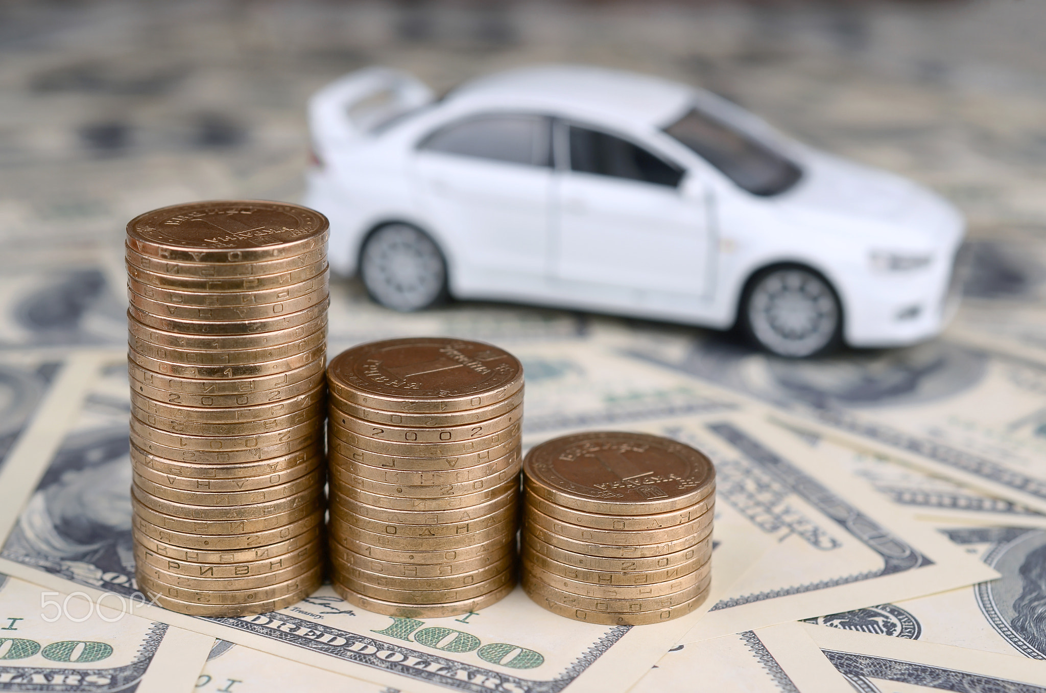 Toy car model at the stacks of golden coins lies on many dollar bills