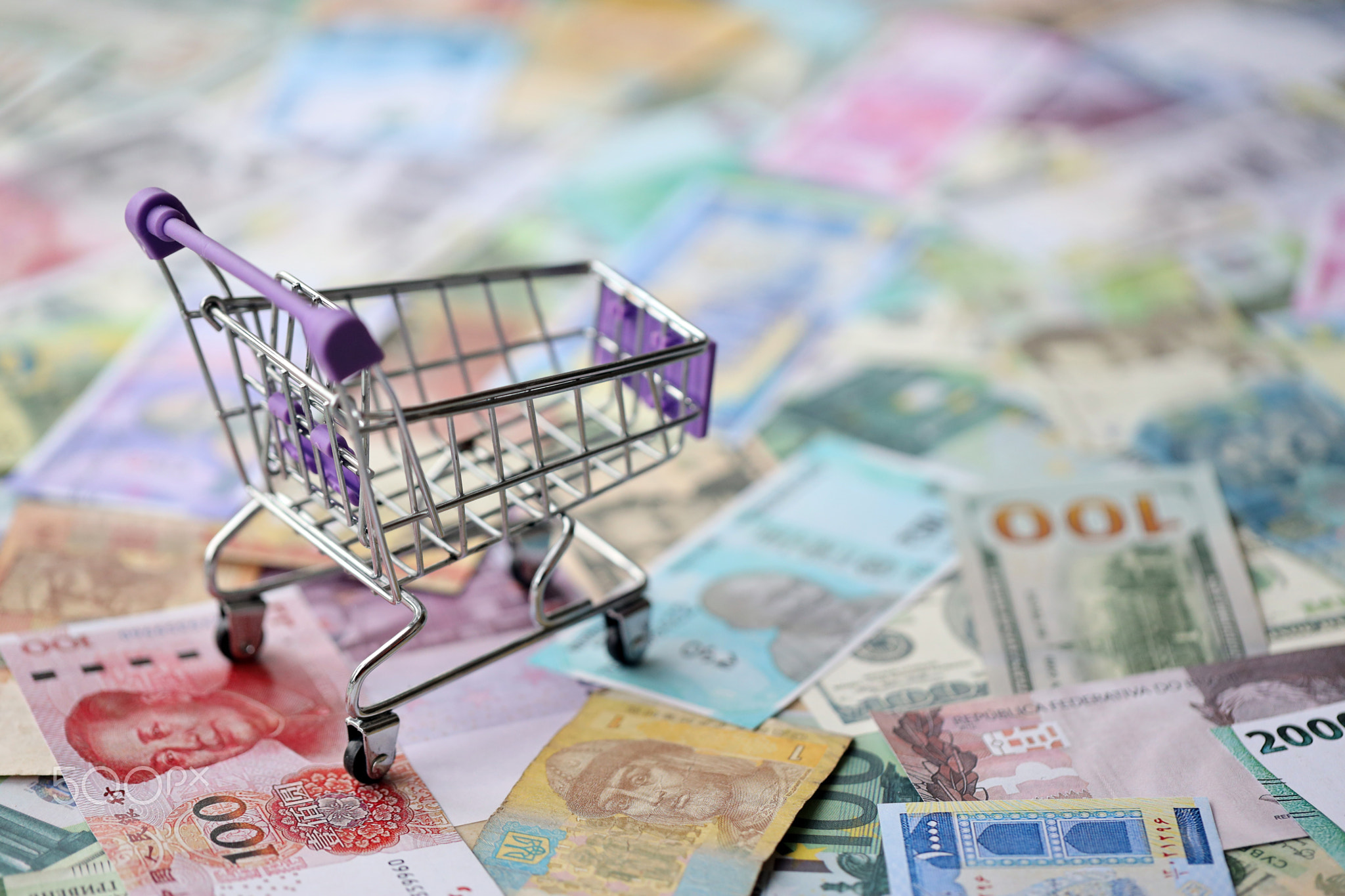 Supermarket trolley on many banknotes of different currency. Background of shopping worldwide