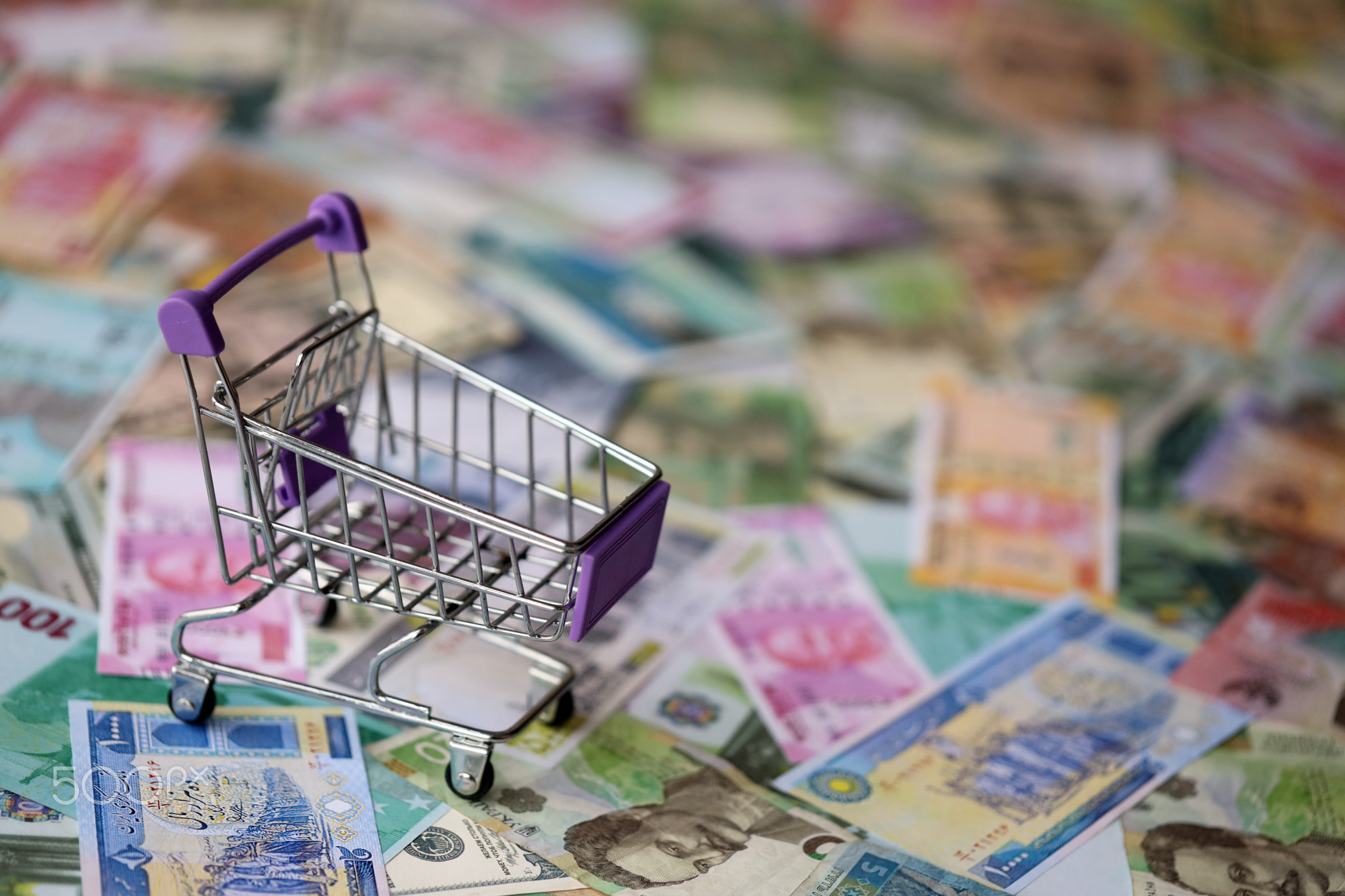 Supermarket trolley on many banknotes of different currency. Background of shopping worldwide