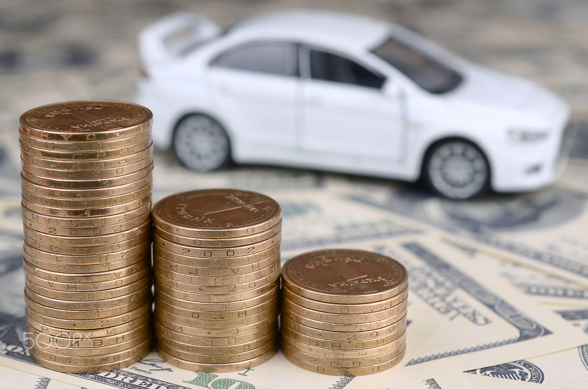 Toy car model at the stacks of golden coins lies on many dollar bills