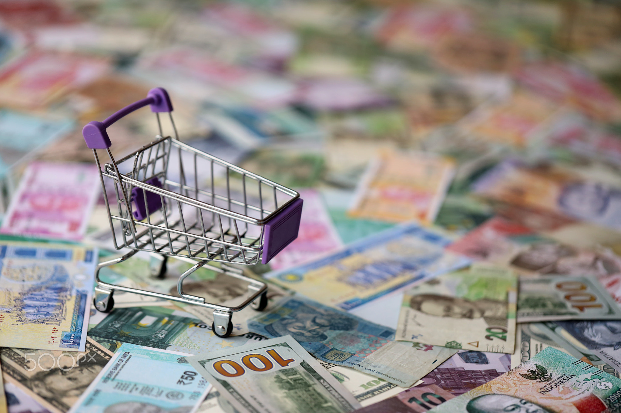 Supermarket trolley on many banknotes of different currency. Background of shopping worldwide