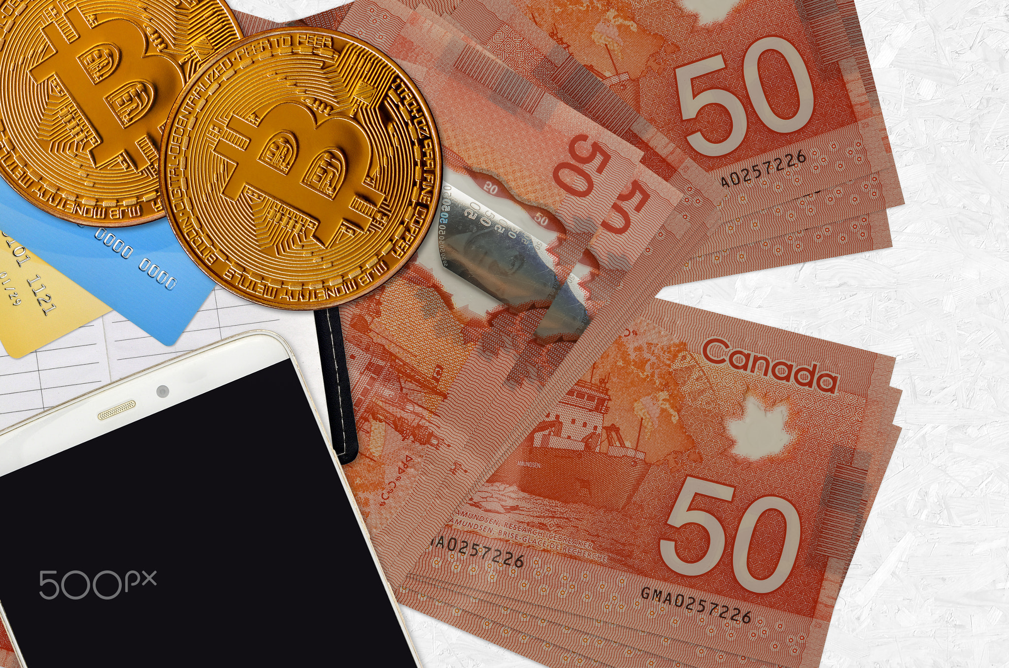 50 Canadian dollars bills and golden bitcoins with smartphone and credit cards. Cryptocurrency