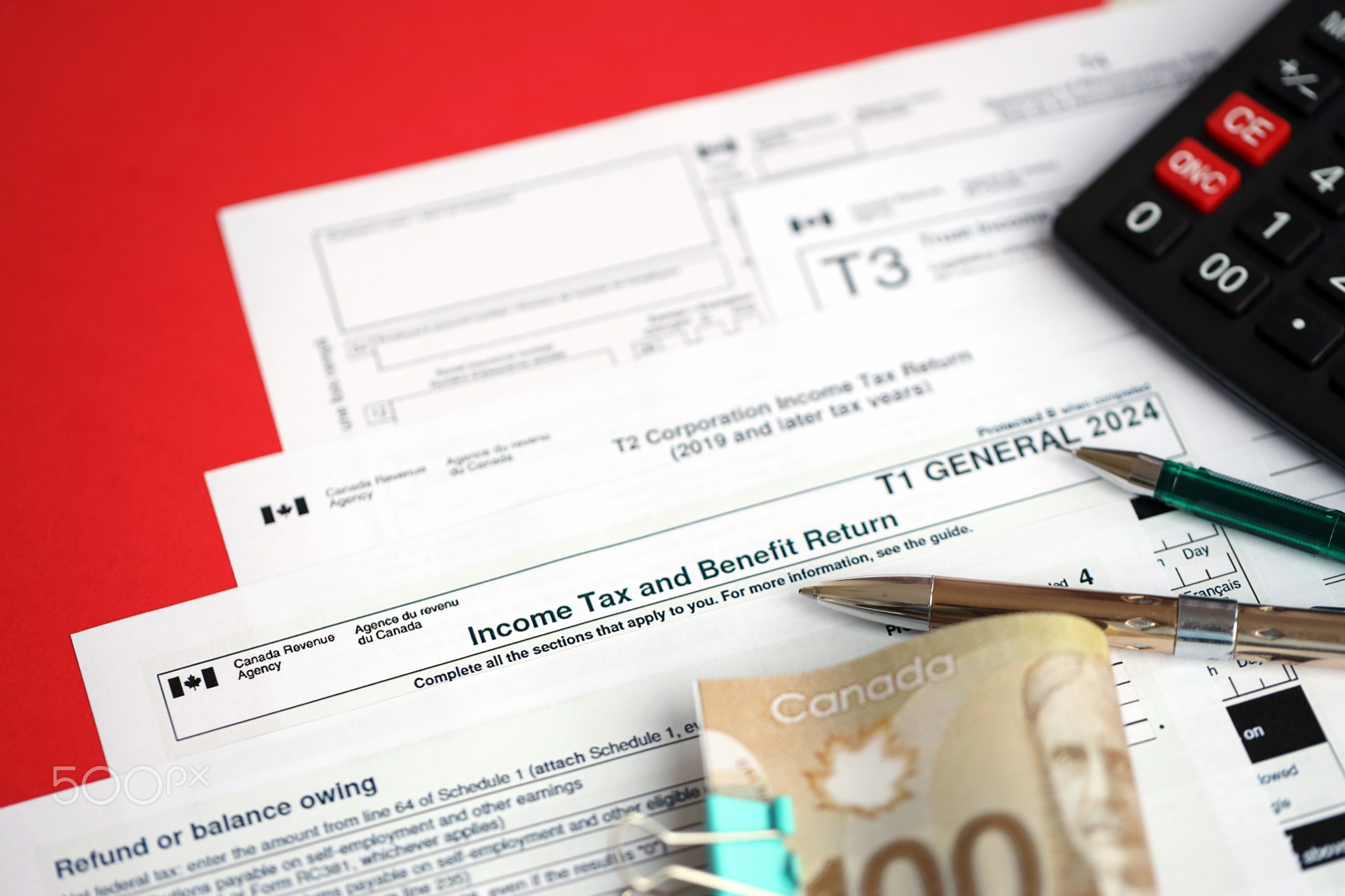 Many blank Canadian tax forms lies on table with canadian money bills, calculator and pen